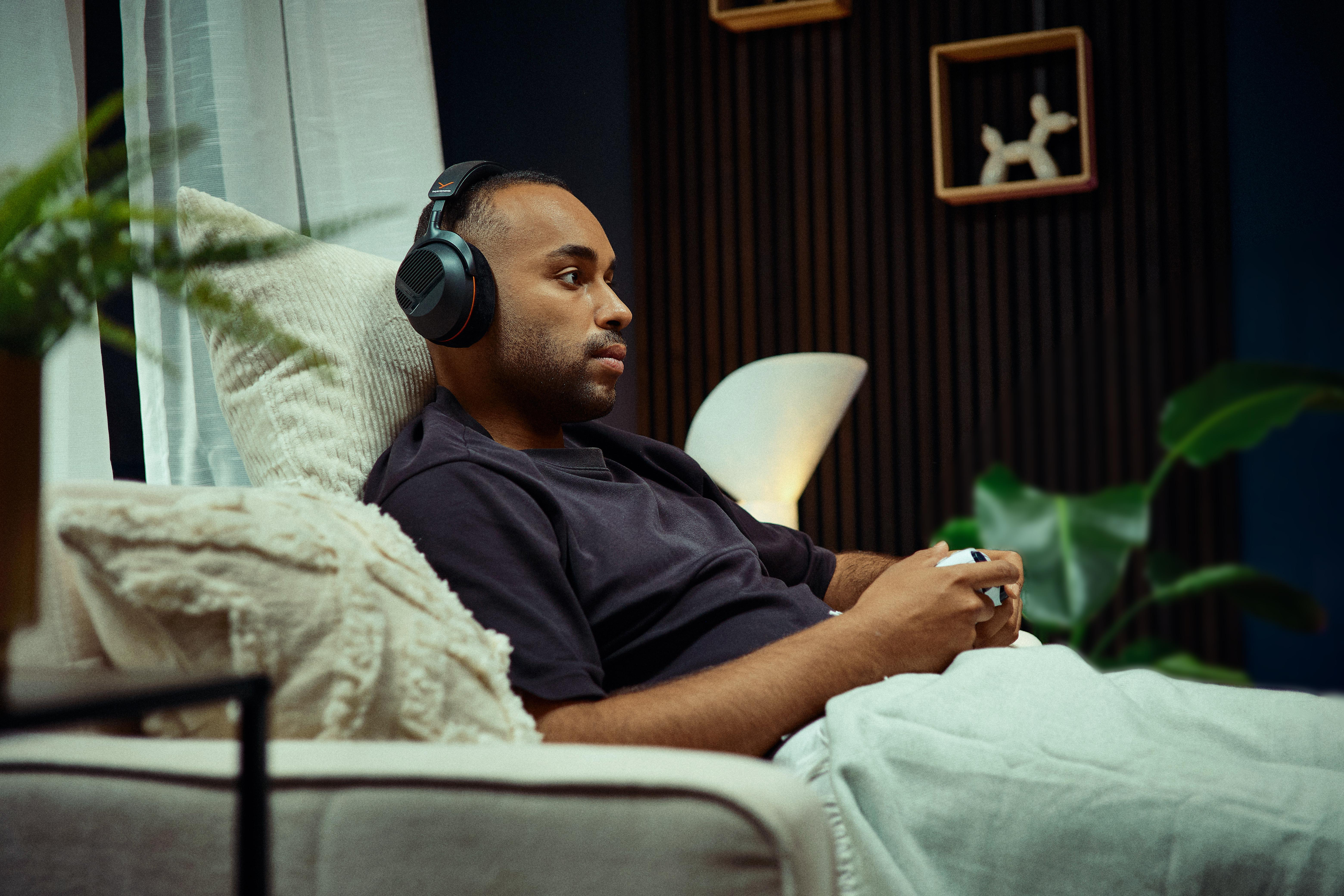 Ein junger Mann sitzt mit Kopfhörern und einem Controller auf dem Sofa und spielt Videospiele.