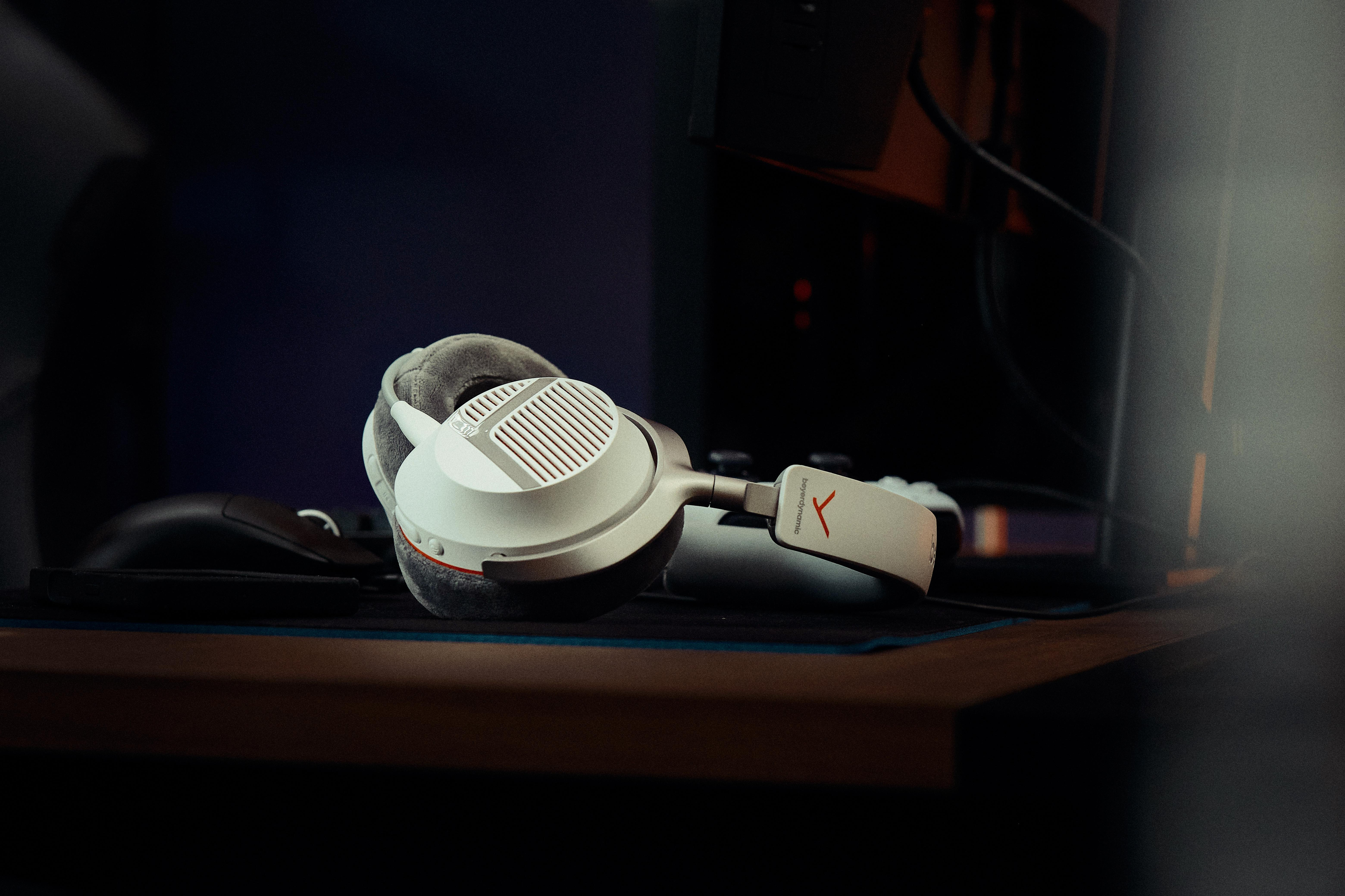 Weiße Beyerdynamic Kopfhörer liegen auf einem dunklen Schreibtisch vor Computerhintergrund.