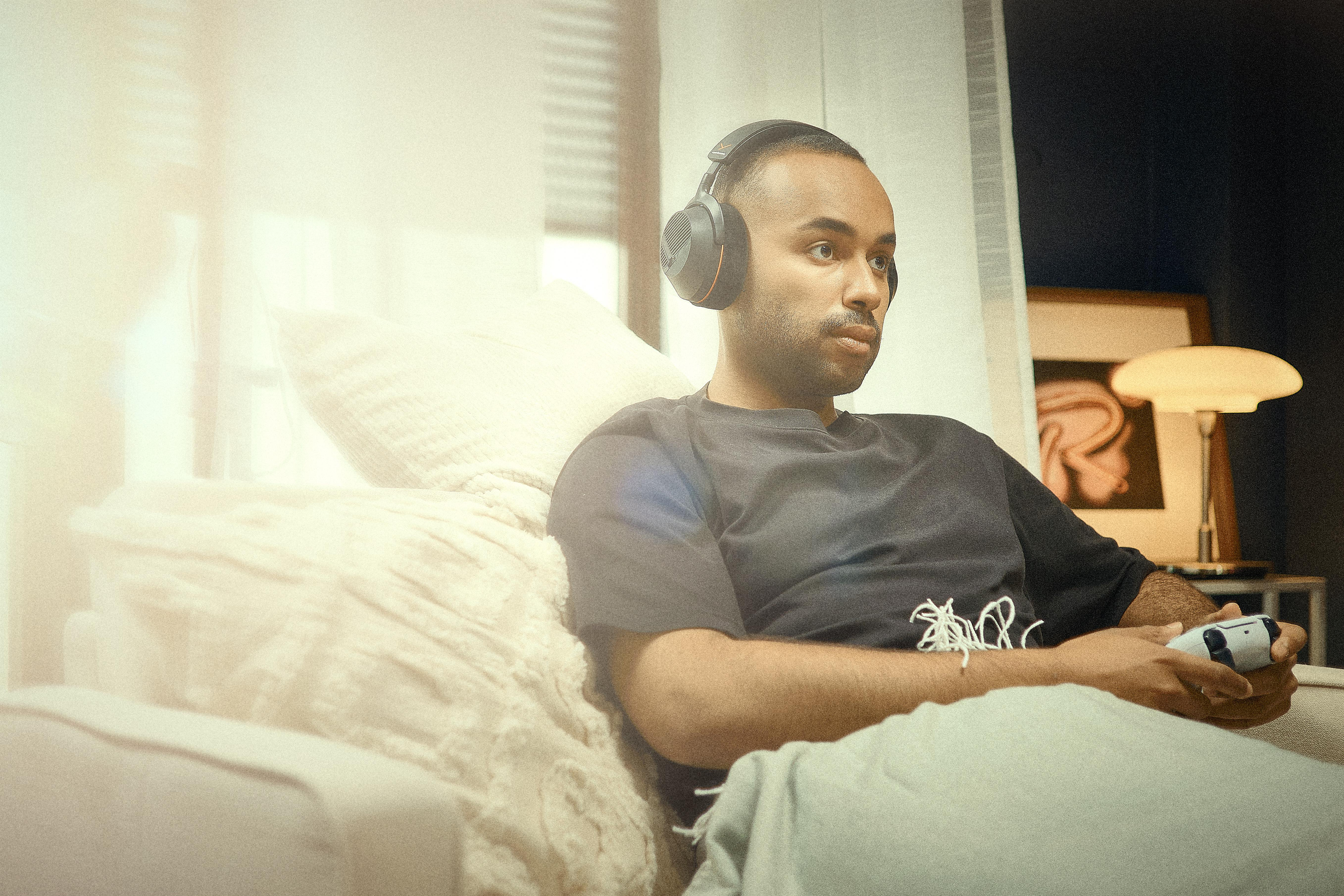 Ein junger Mann mit Kopfhörern sitzt auf einem Sofa und spielt Videospiele.