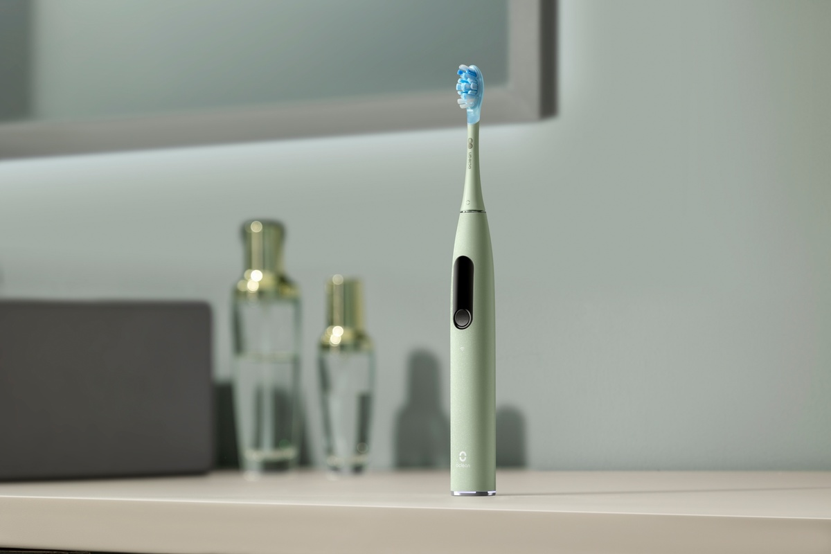 Eine hellgrüne elektrische Zahnbürste steht auf einer Badezimmertheke mit zwei Glasflaschen im verschwommenen Hintergrund.