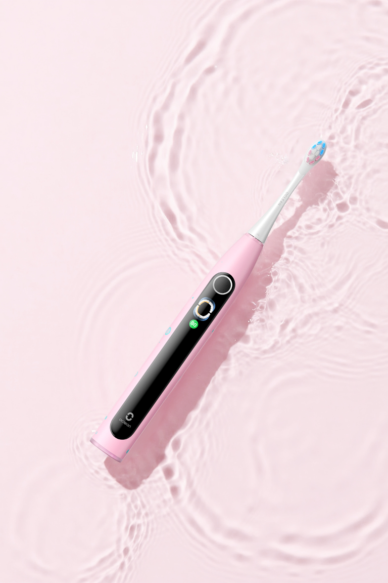 Eine rosa elektrische Zahnbürste liegt schräg auf einer hellrosa Wasseroberfläche mit leichten Wellen.