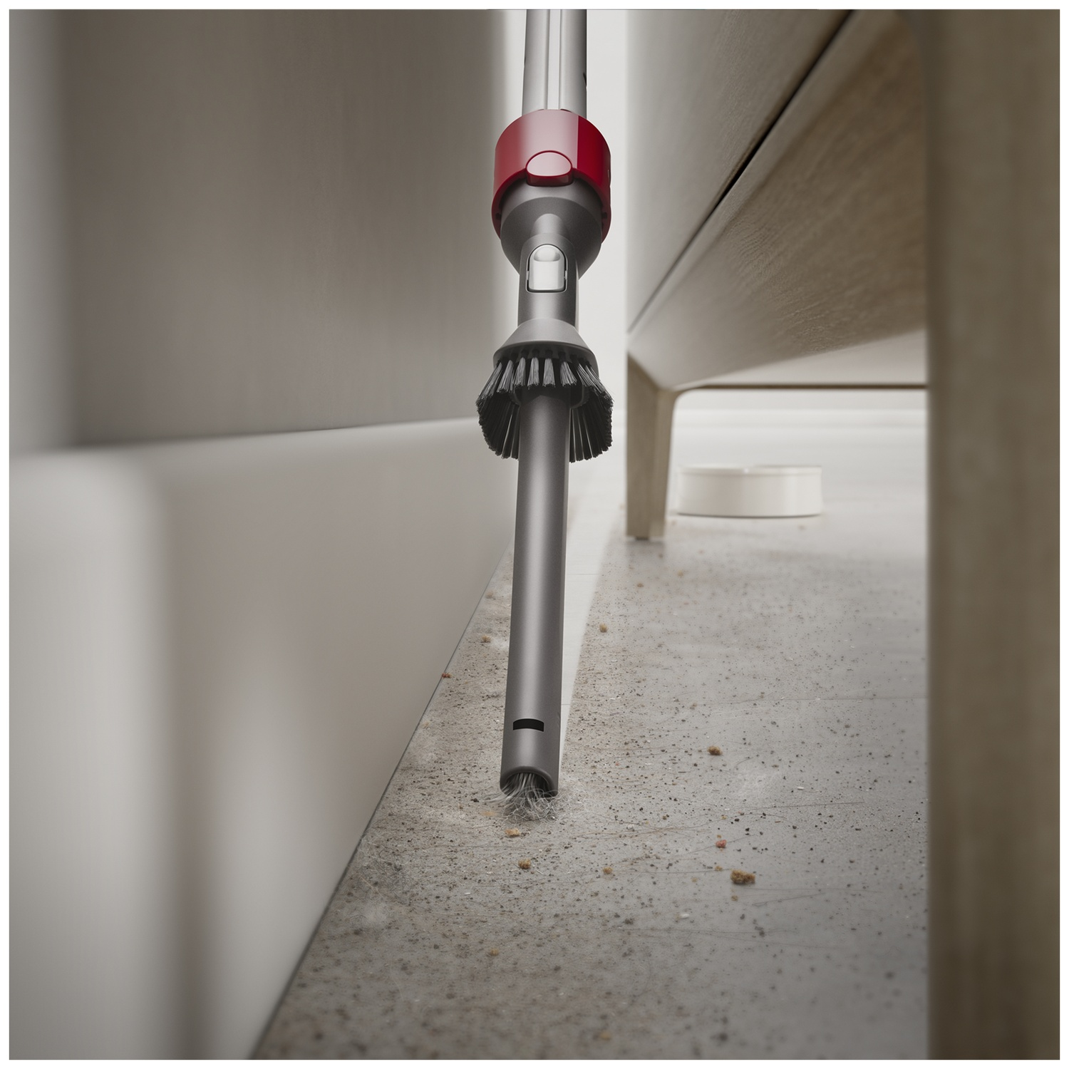 A vacuum cleaner attachment with red and grey details cleans dirt and dust off the floor near a wall.