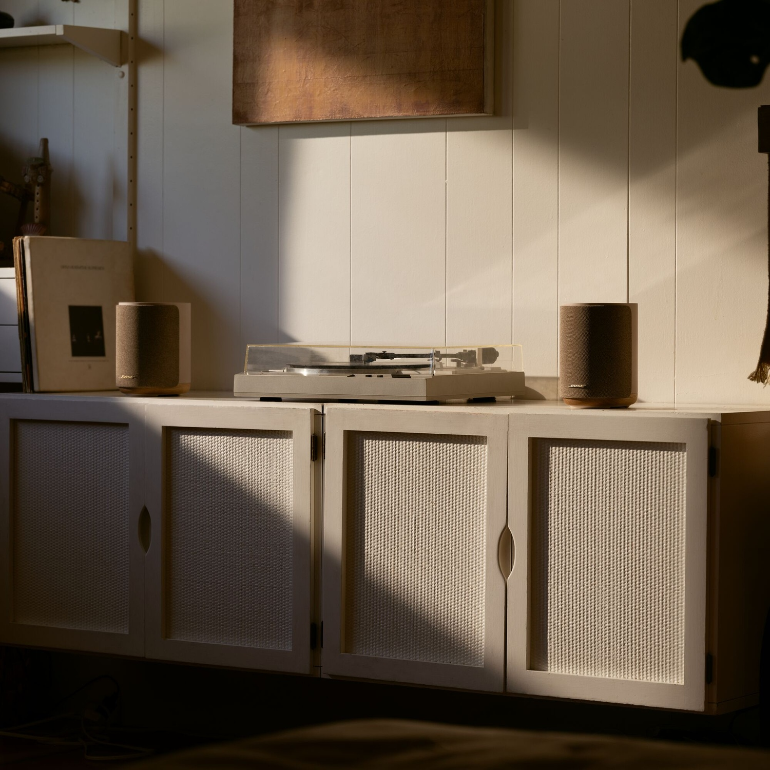 A turntable and two speakers on a white cabinet against a paneled wall with warm sunlight streaming across.