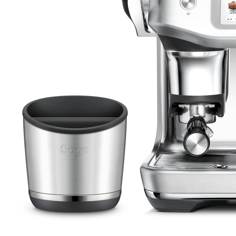 Eine silberne Sage-Abschlagbox steht neben einer modernen Kaffeemaschine auf weißem Hintergrund.