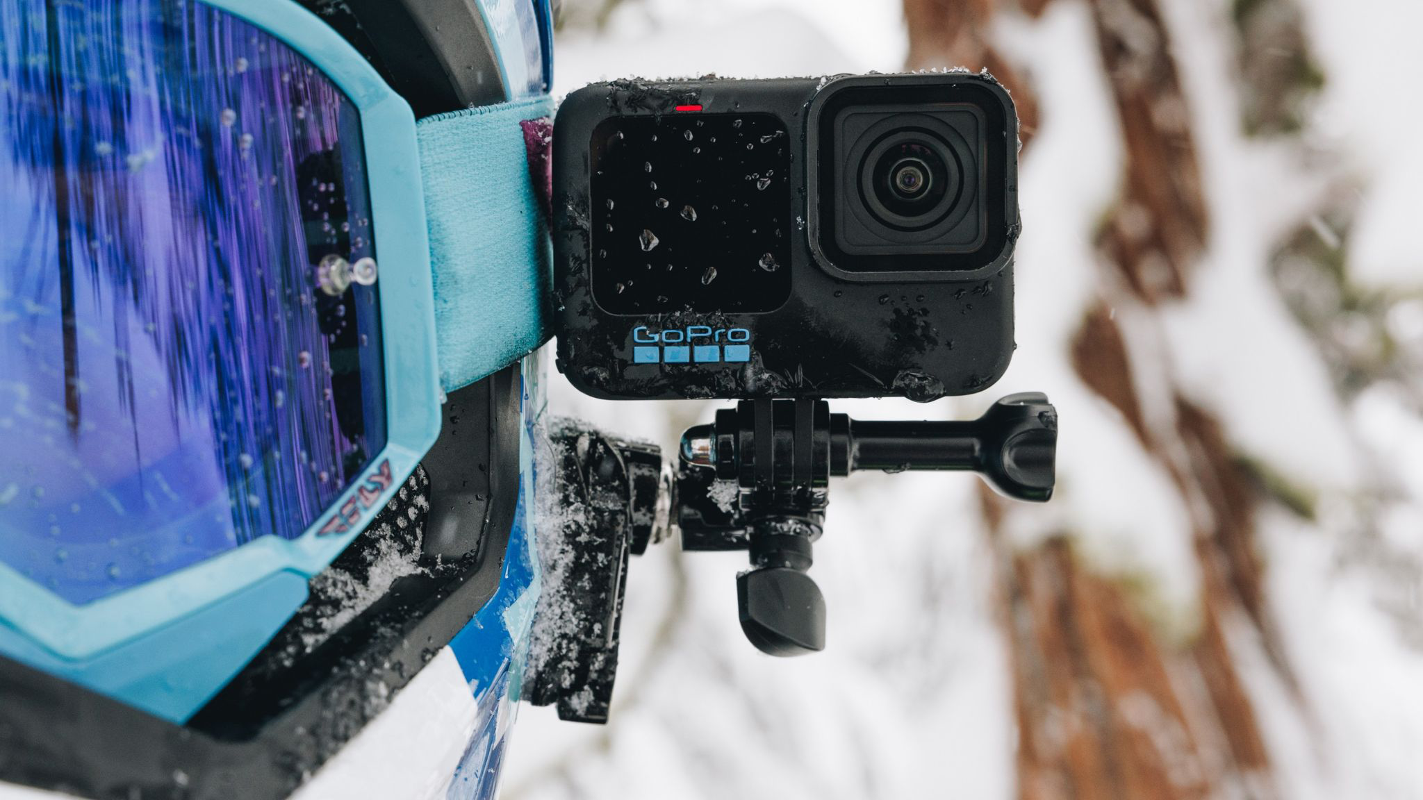 GoPro kamera sísisakra szerelve, kék síszemüveggel, havas háttérrel.