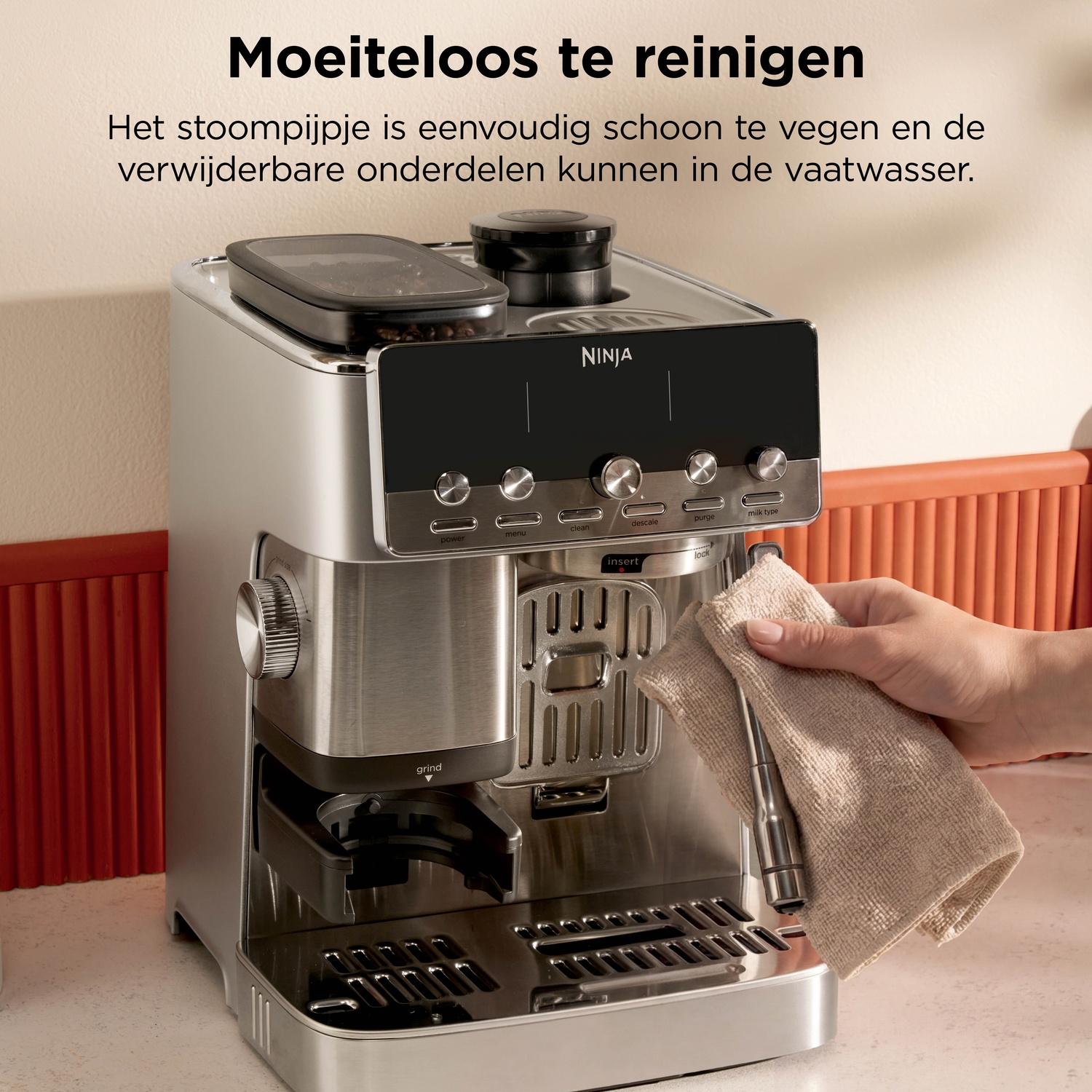 A hand wiping down the steam wand of a silver Ninja espresso machine with a cloth.