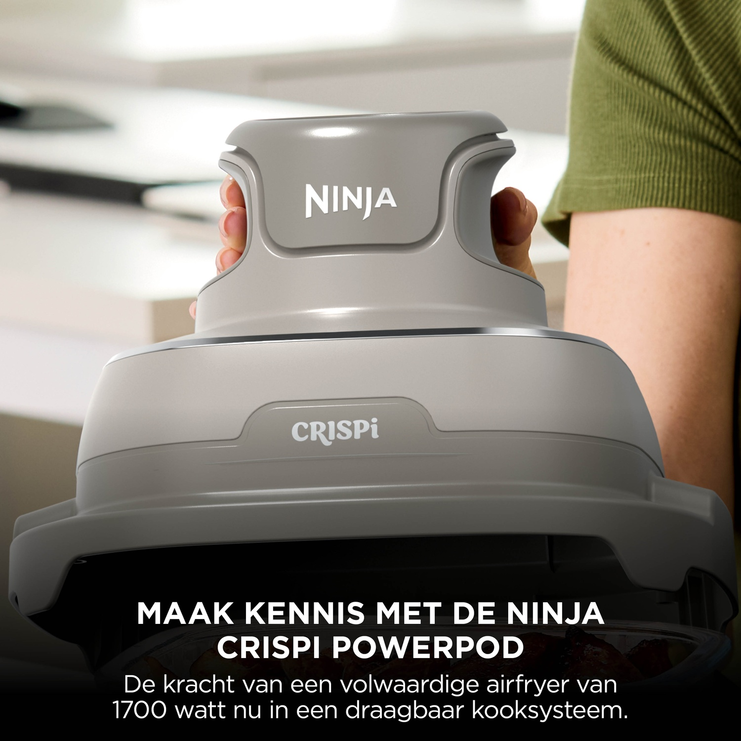 Person holding a grey Ninja Crispi Powerpod cooking unit in a kitchen.