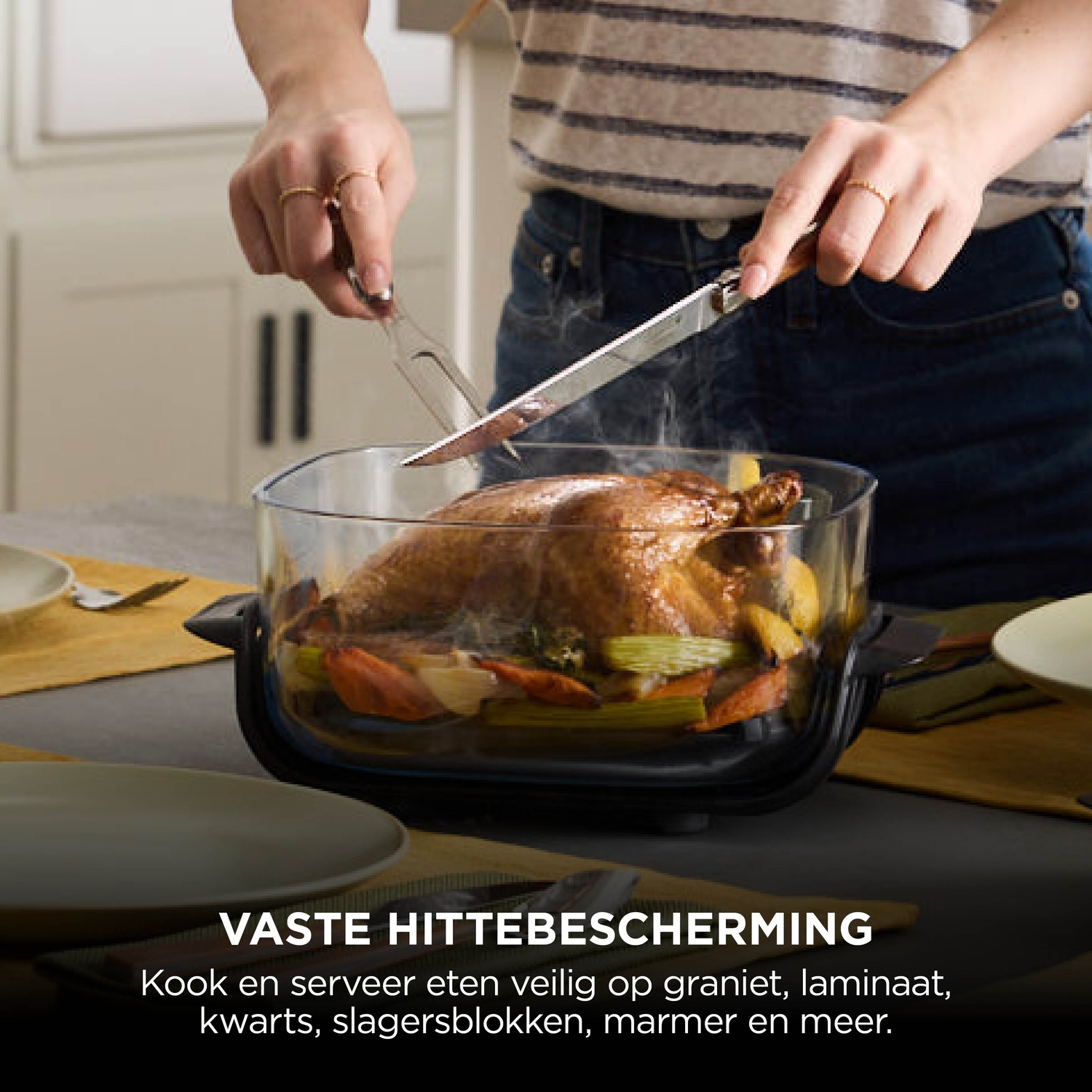 A person uses a knife and fork to carve a roasted chicken with vegetables in a clear glass dish on a table.