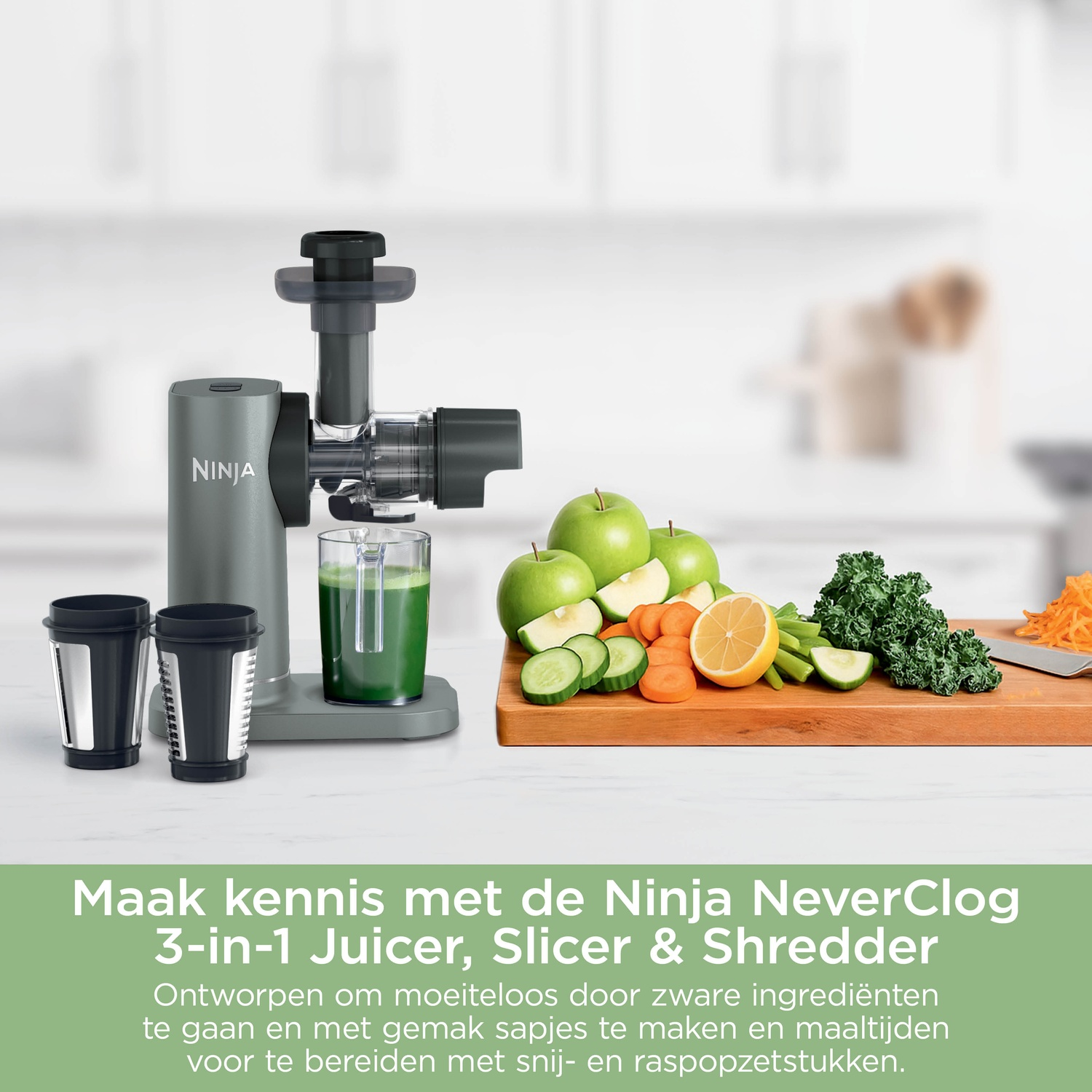 A grey Ninja juicer next to a cutting board with green apples, sliced cucumbers, carrots, a lemon, and kale.