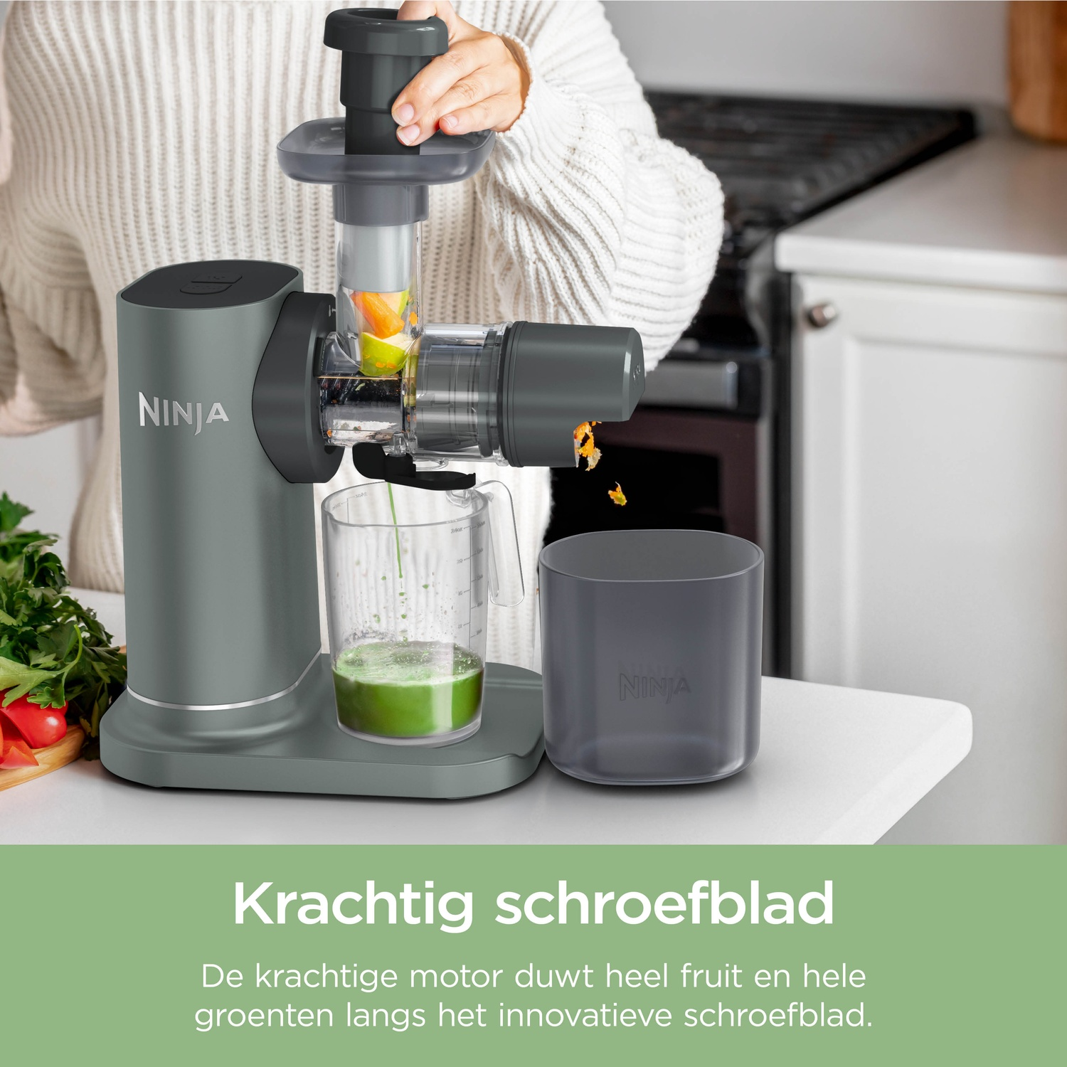 A person uses a grey Ninja slow juicer on a white kitchen counter, extracting green juice into a pitcher.