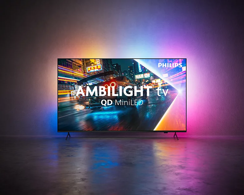 Ein Philips Ambilight QD MiniLED Fernseher auf einem Boden mit bunten Lichtern und einem Auto auf dem Bildschirm.
