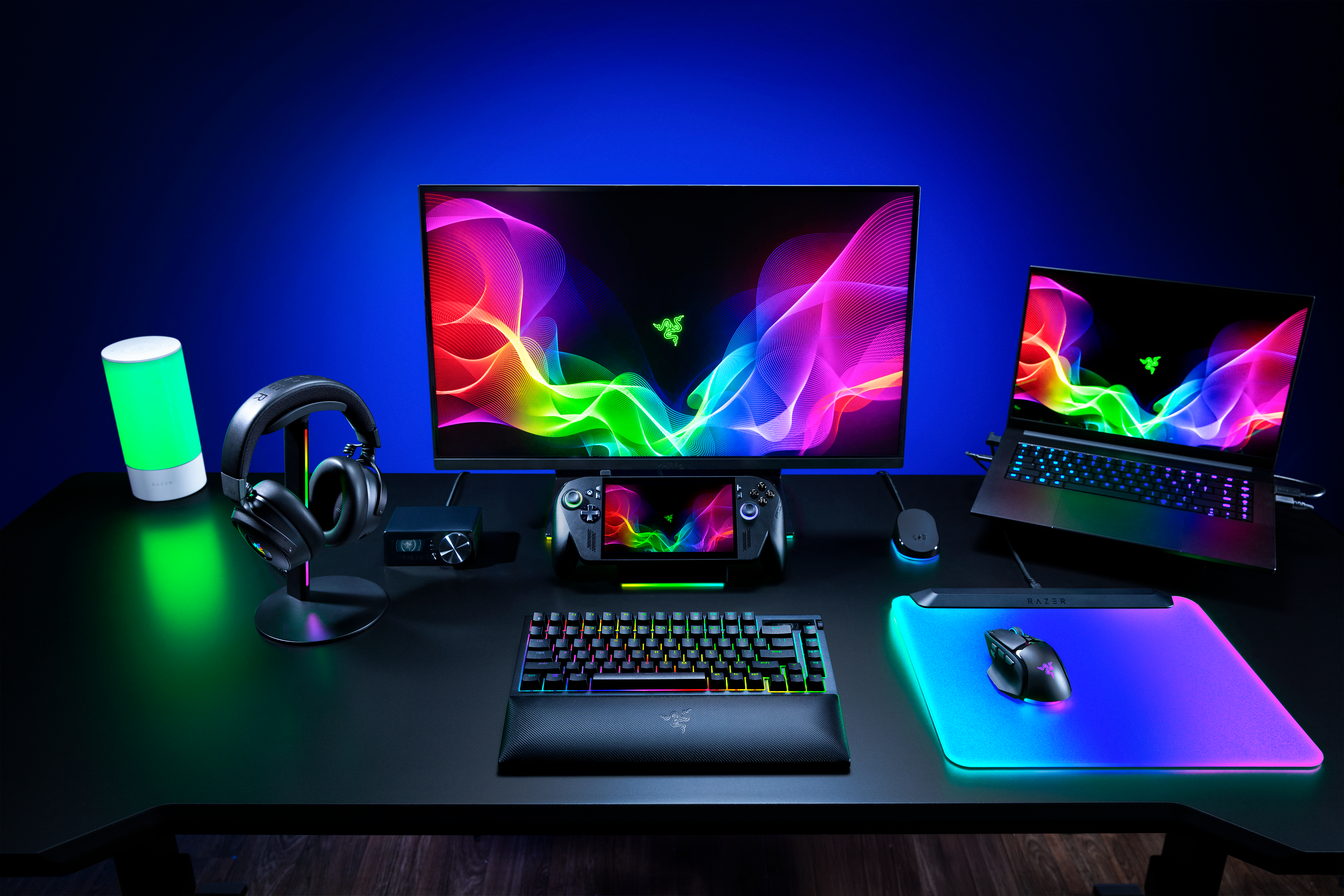 Ein Gaming-Schreibtisch mit Monitor, Laptop, Tastatur, Maus und Kopfhörern, beleuchtet mit bunten RGB-Lichern.