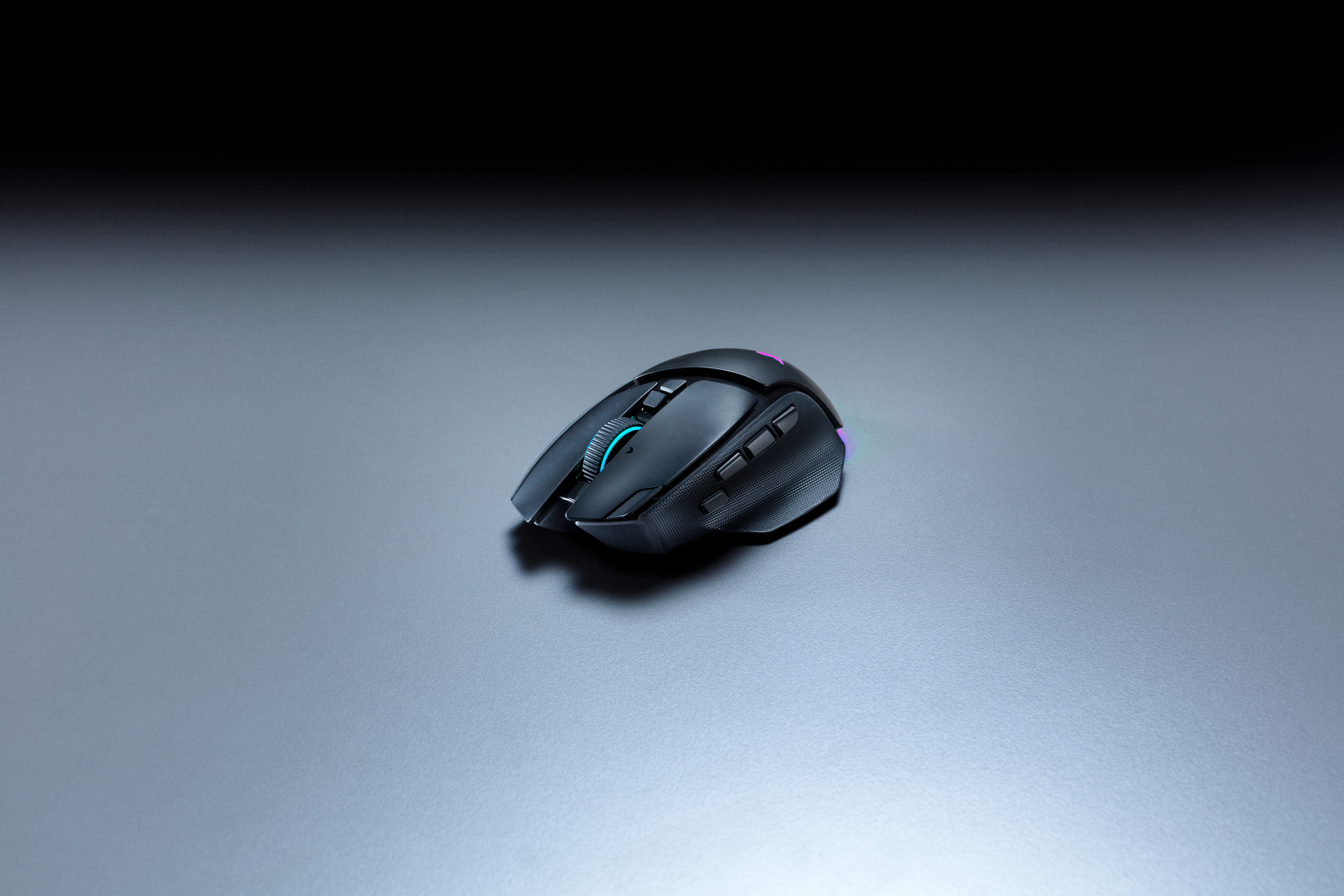 Eine schwarze Computermaus mit blauer Beleuchtung steht auf einer grauen Oberfläche vor dunklem Hintergrund.