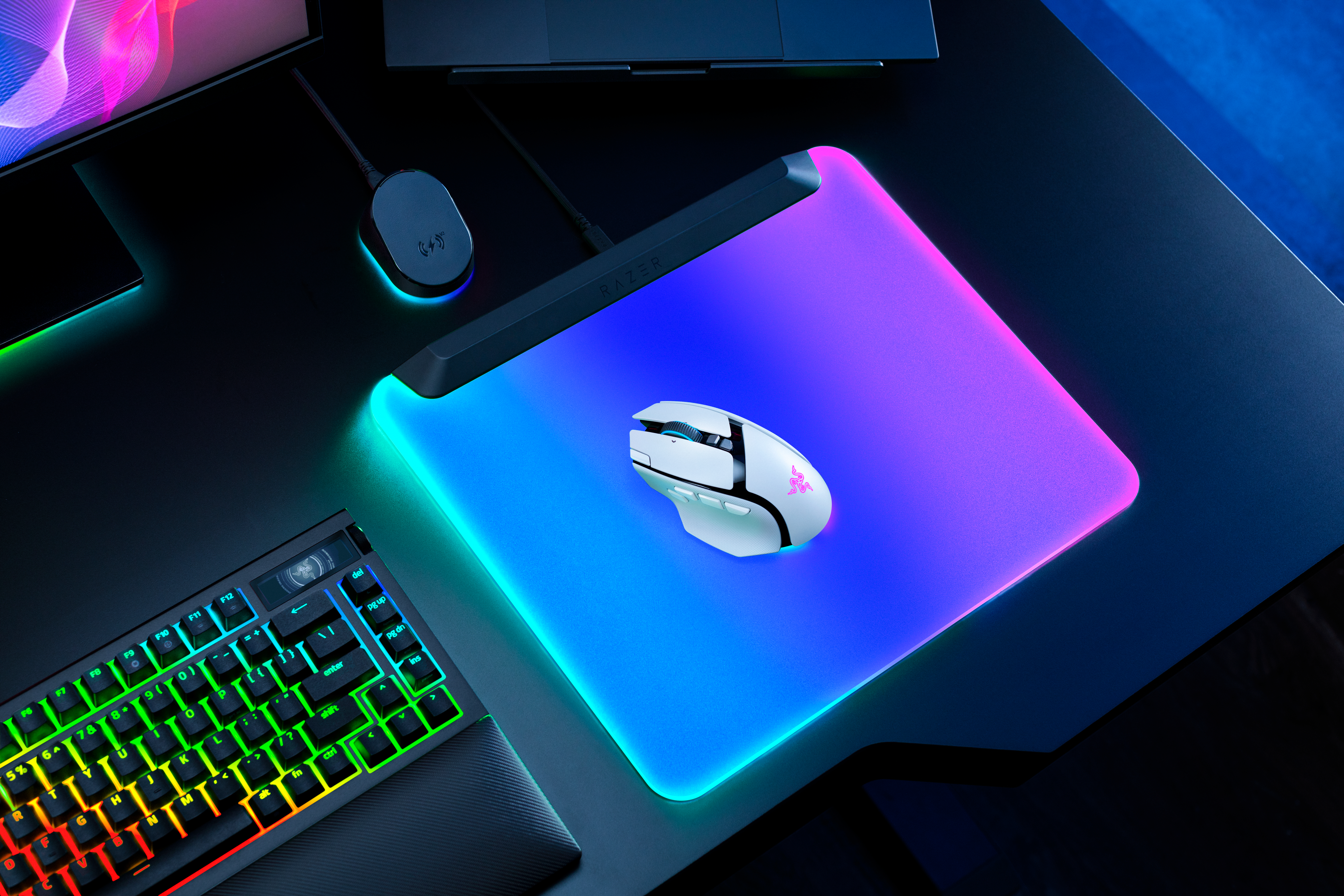 Eine weiße Gaming-Maus und ein leuchtendes Mauspad auf einem schwarzen Schreibtisch neben einer Tastatur.