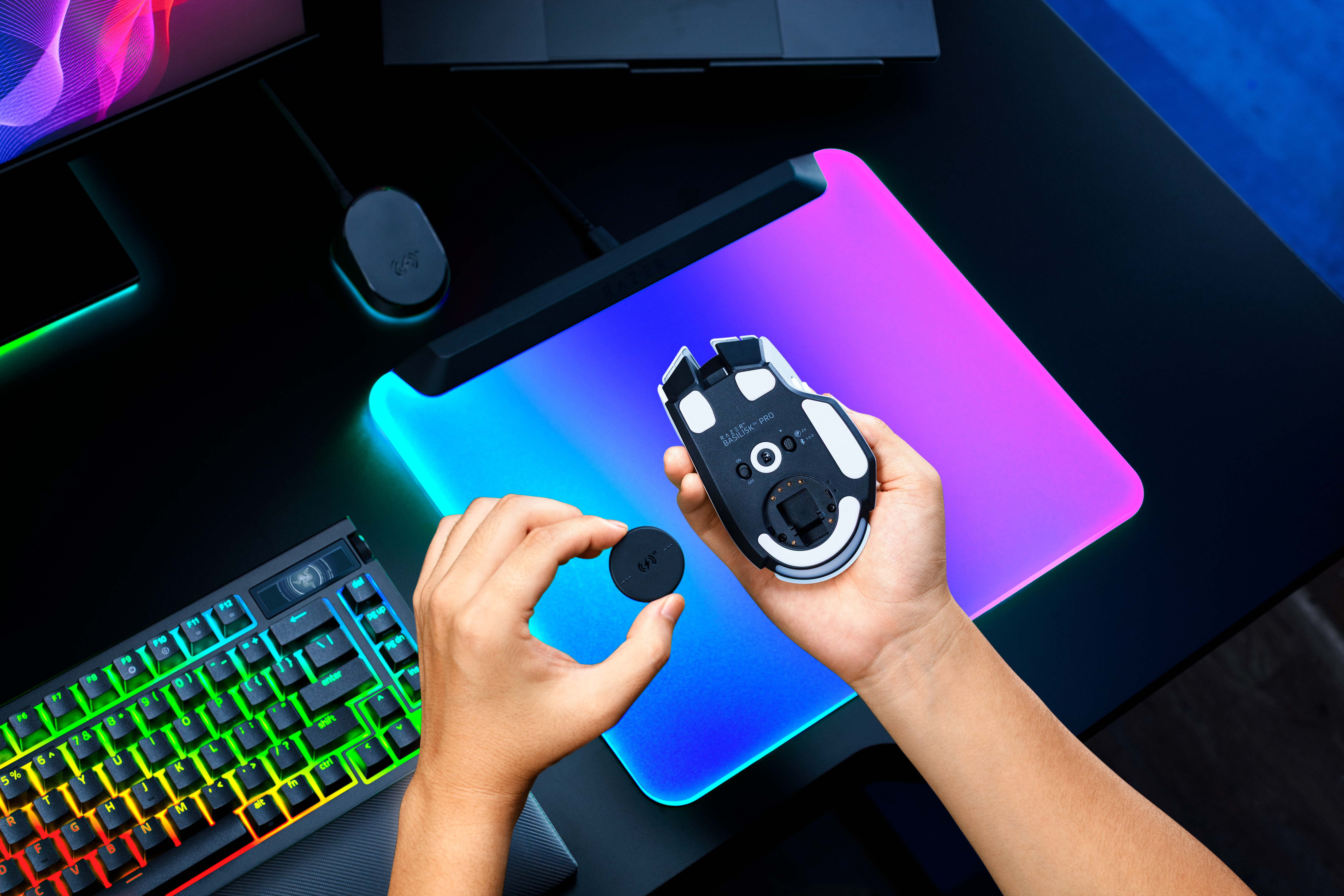 Person hält eine Gaming-Maus und ein kleines rundes Bauteil über einem beleuchteten Mauspad.