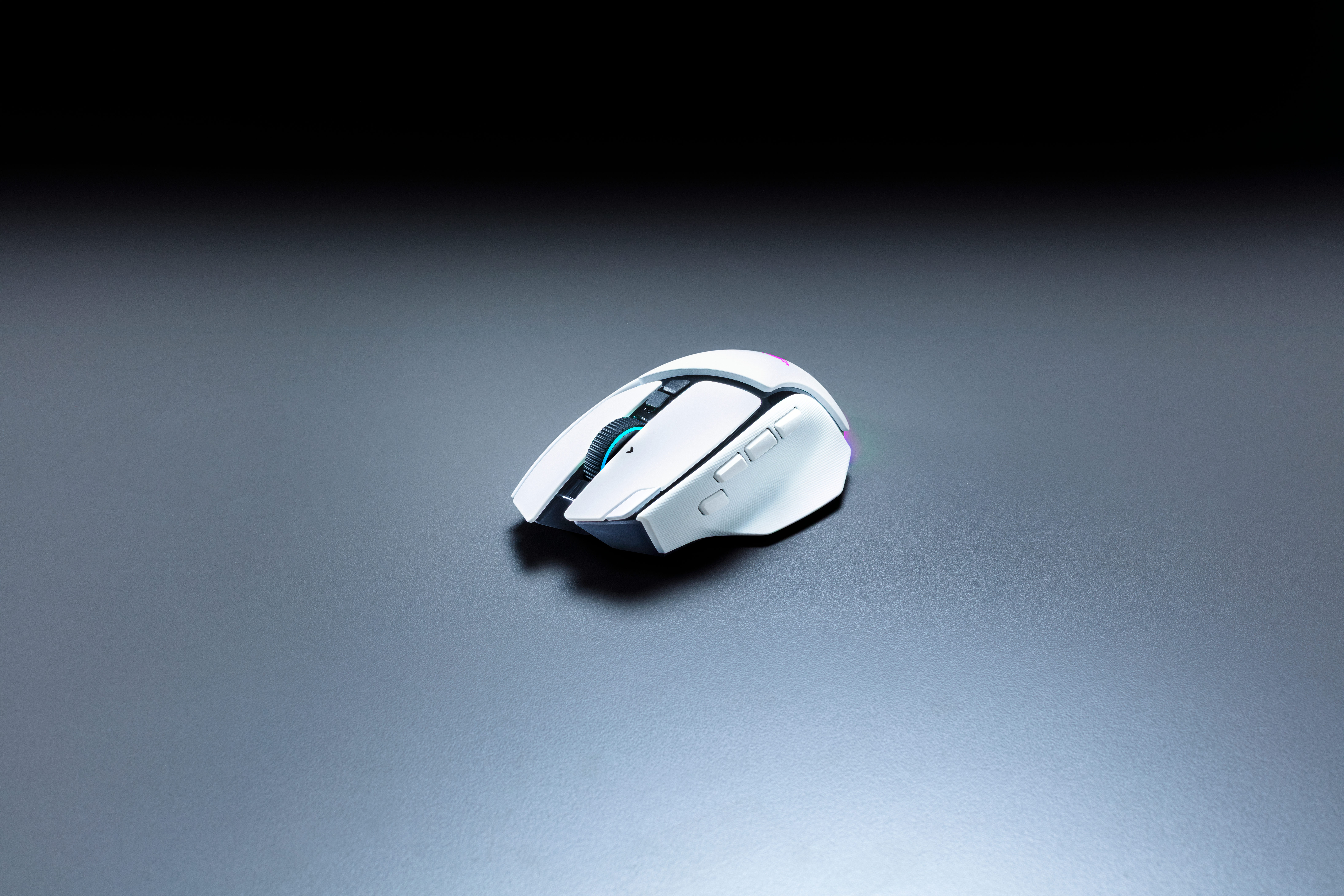 Eine weiße Gaming-Maus mit RGB-Beleuchtung auf einer grauen Oberfläche vor dunklem Hintergrund.