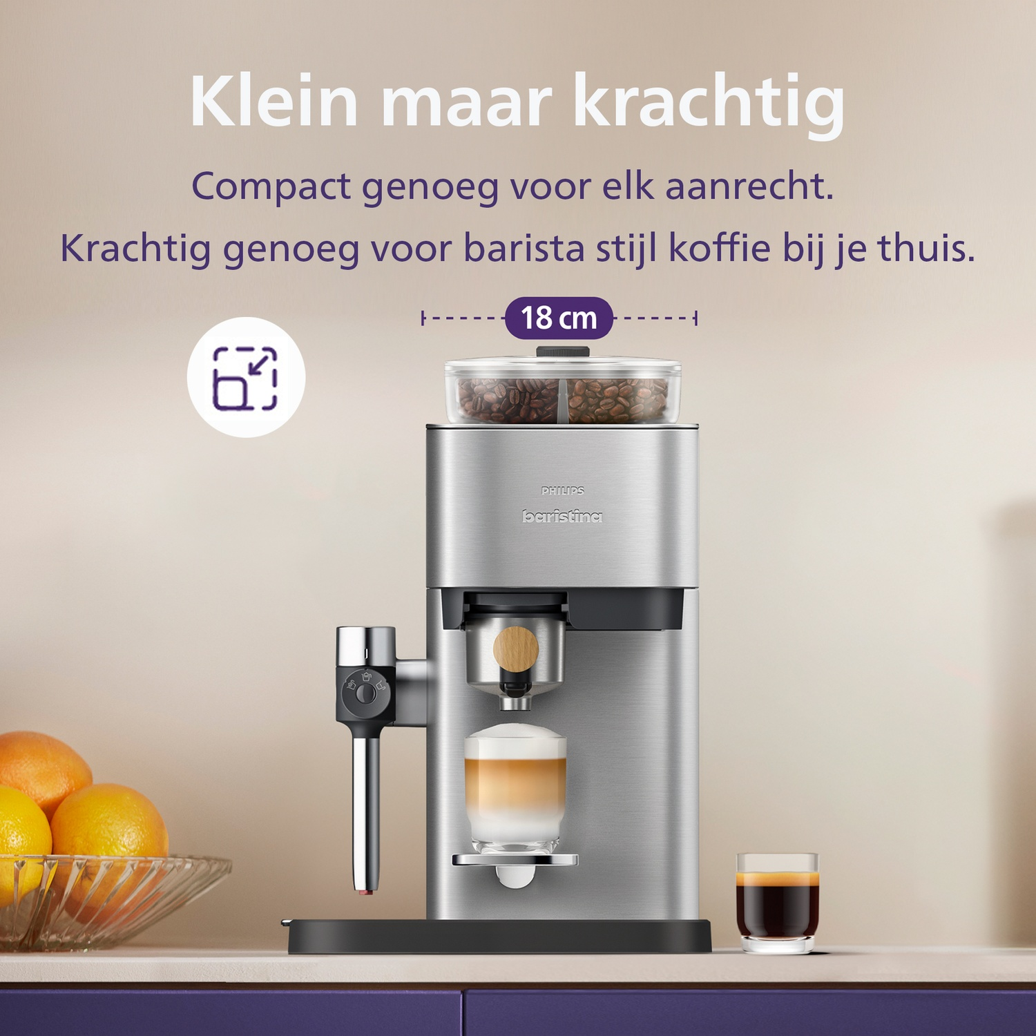 Compact silver Philips Baristina coffee machine on a counter with fresh oranges and coffee cups.