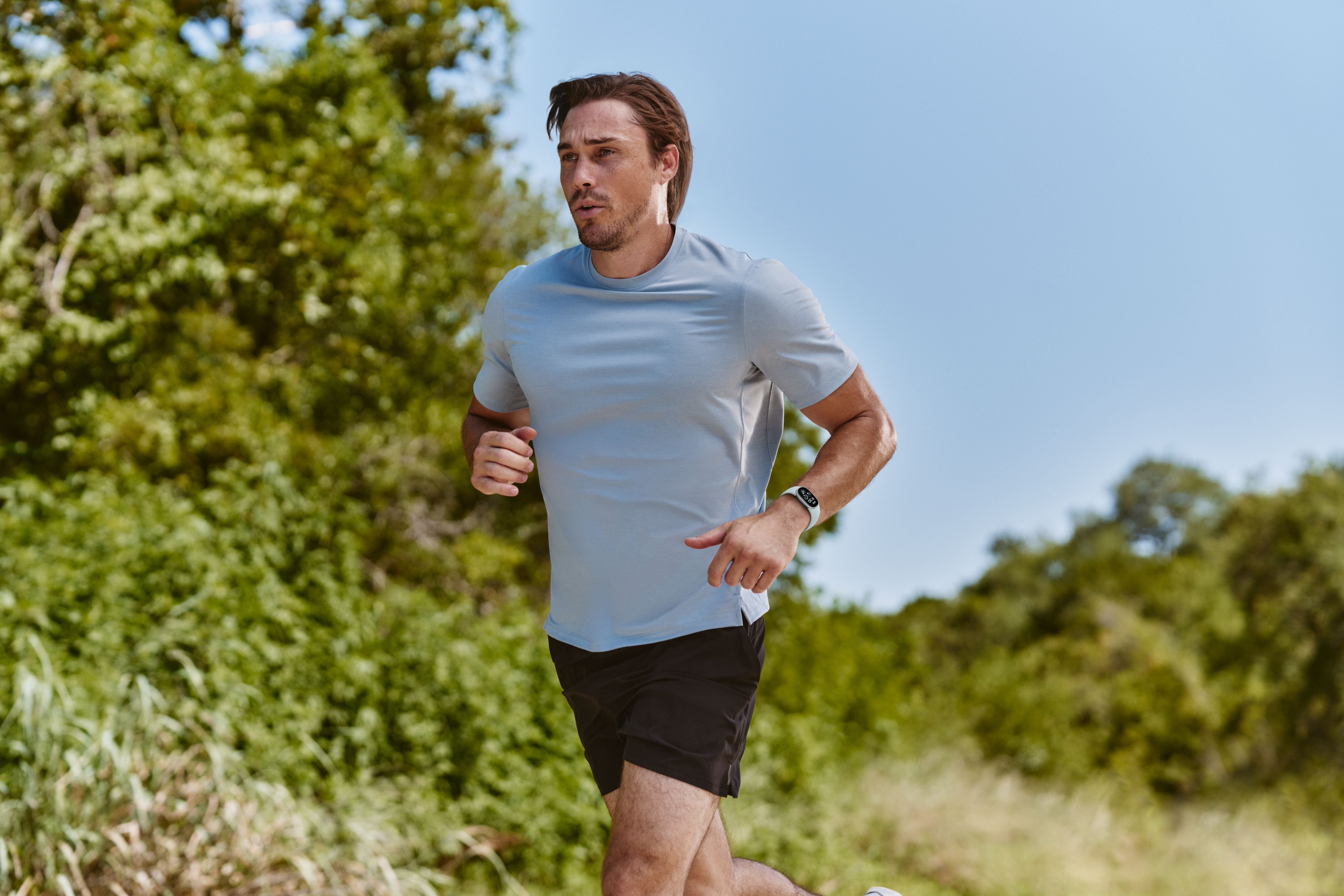Ein Mann im hellblauen T-Shirt und schwarzen Shorts läuft auf einem grünen, sonnigen Pfad.