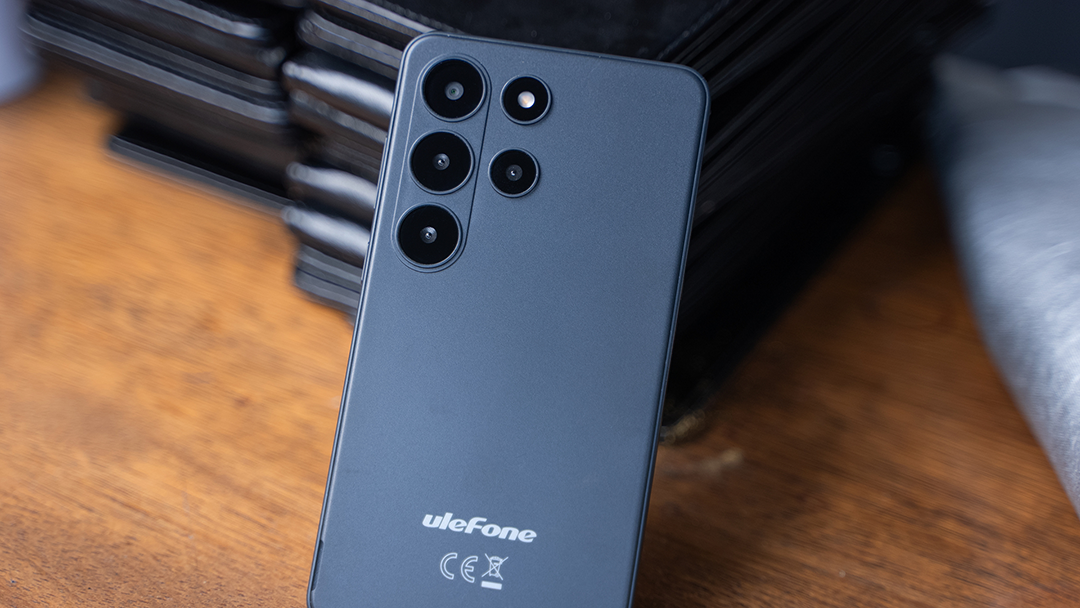 Sötétszürke Ulefone okostelefon fa felületen, halmozott tokok előtt.