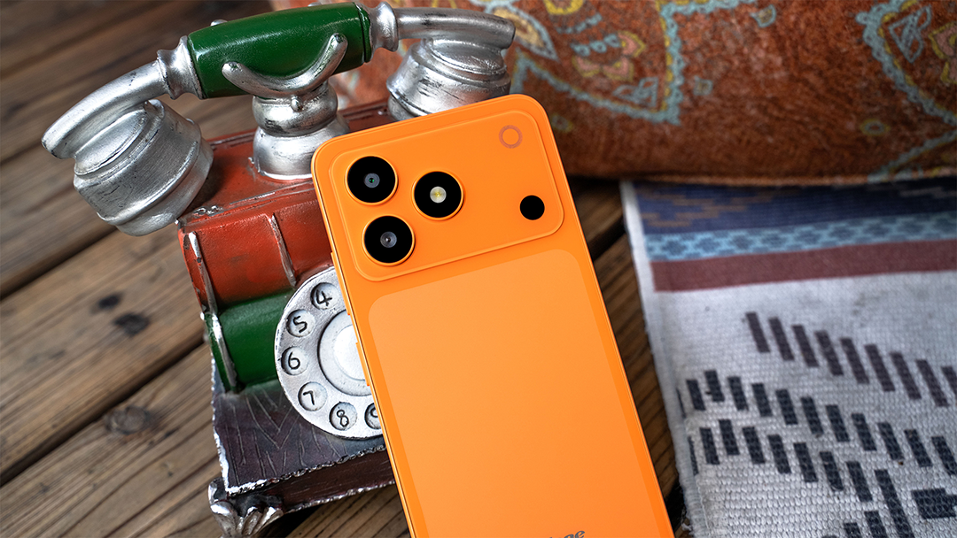 Egy élénk narancssárga okostelefon fekszik egy régi játéktelefon előtt egy faasztalon.