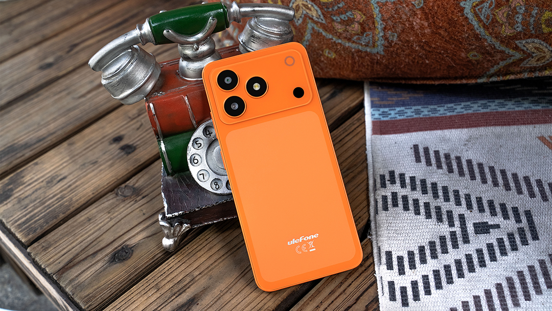 Egy élénk narancssárga Ulefone okostelefon fekszik falemezeken egy antik telefon és egy mintás takaró előtt.