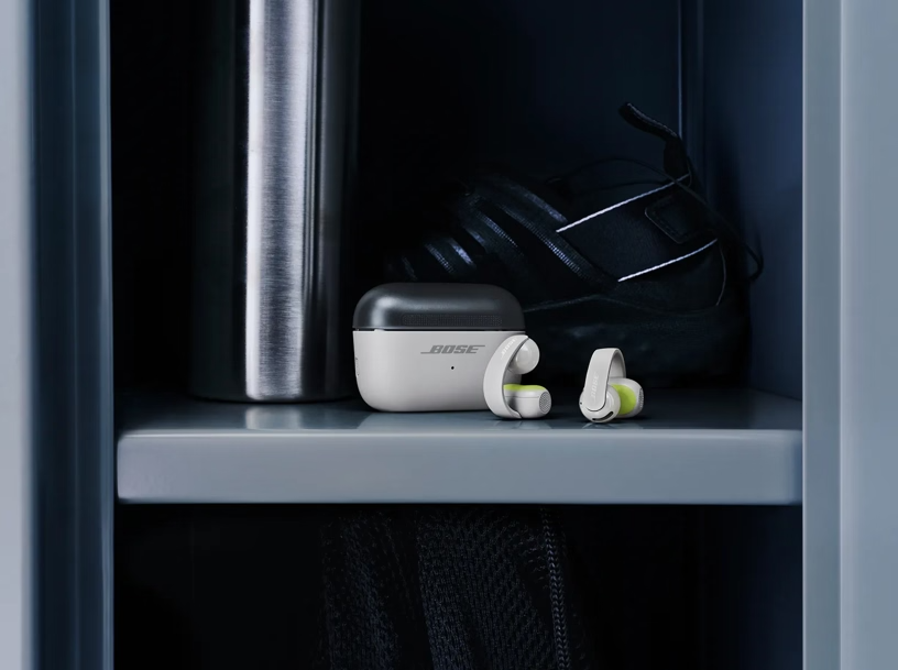 Bose fülhallgató és töltőtok egy polcon egy vizespalack és egy fekete cipő mellett.