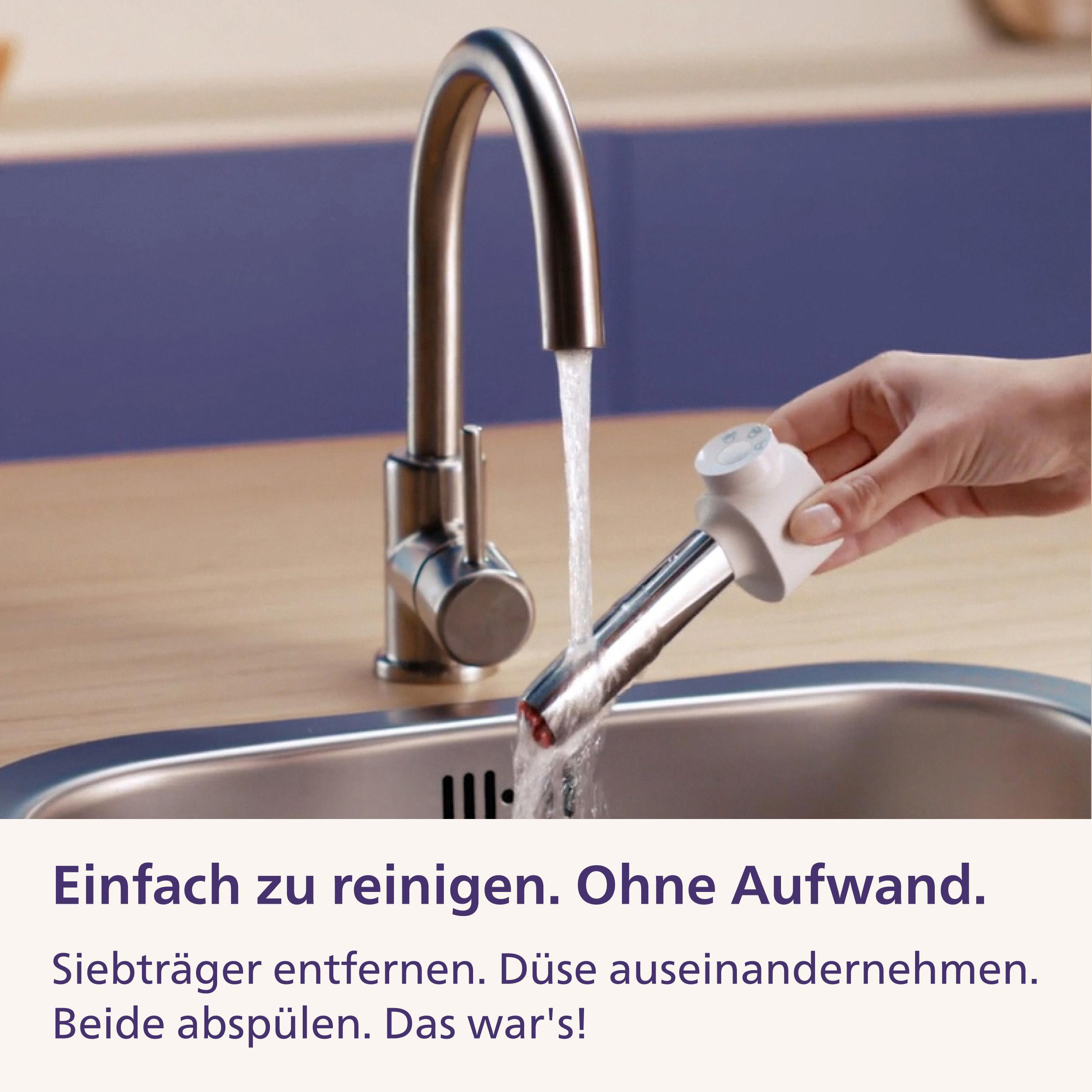 Eine Hand wäscht ein Kaffeemaschinenteil unter einem Chrom-Wasserhahn über einem Edelstahlbecken.