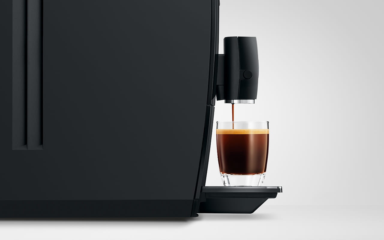 Czarny ekspres do kawy parzy espresso do małej szklanki na jasnej powierzchni.