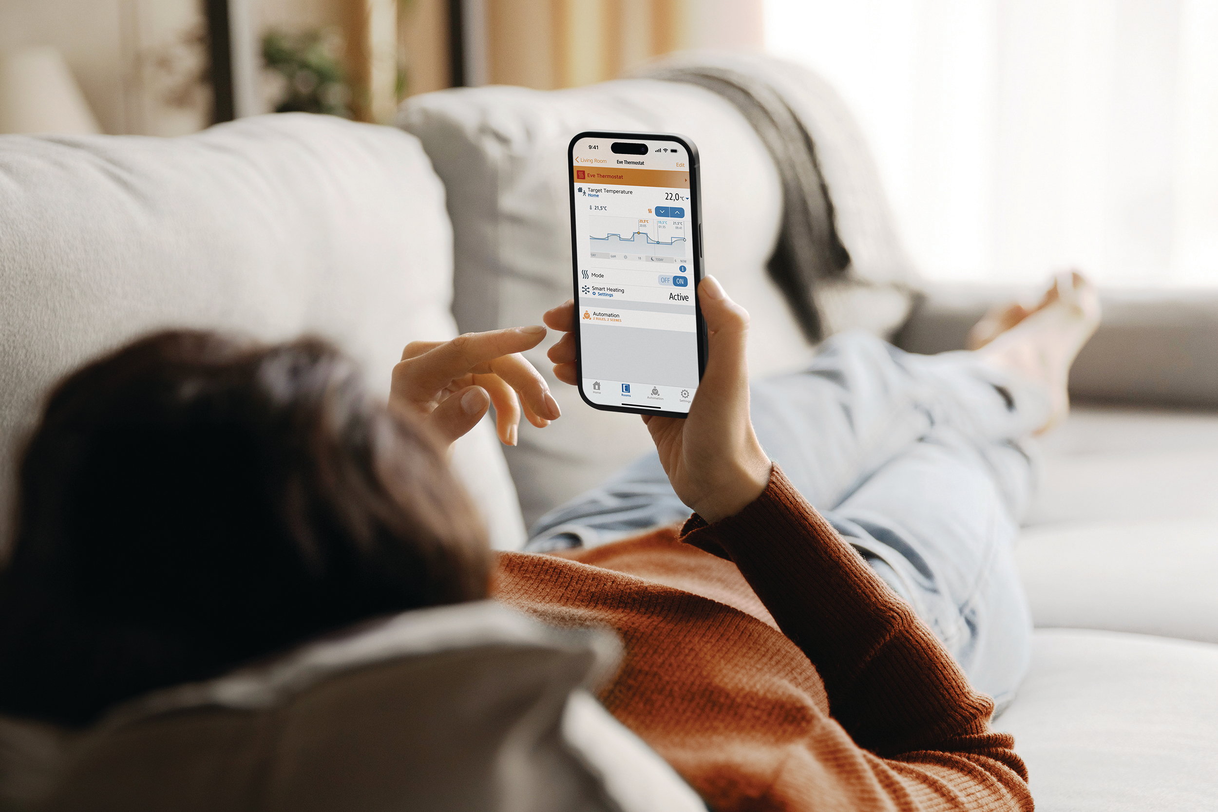 Eine Person liegt auf einem Sofa und steuert die Heizung per Smartphone-App.