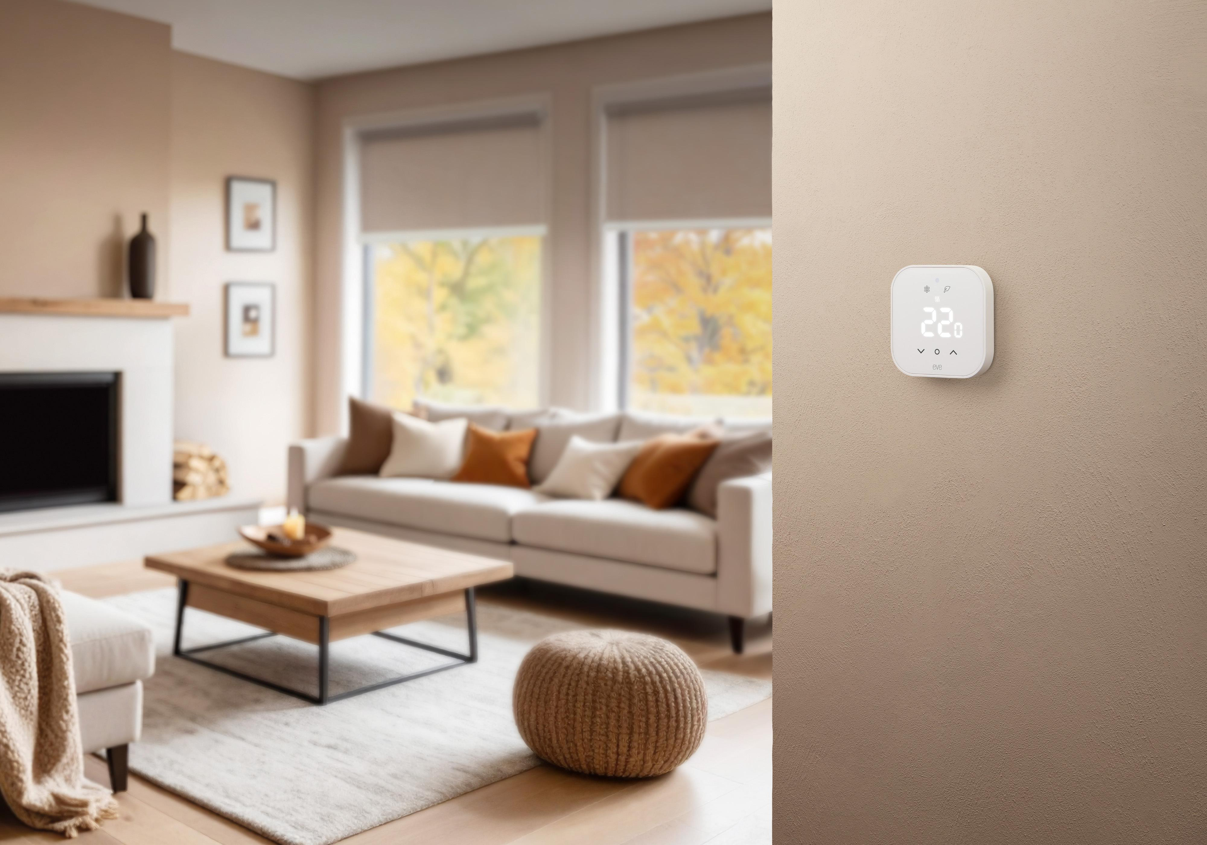 Ein weißer Smart-Thermostat hängt an einer beigen Wand in einem modern eingerichteten Wohnzimmer mit Sofa und Kamin.