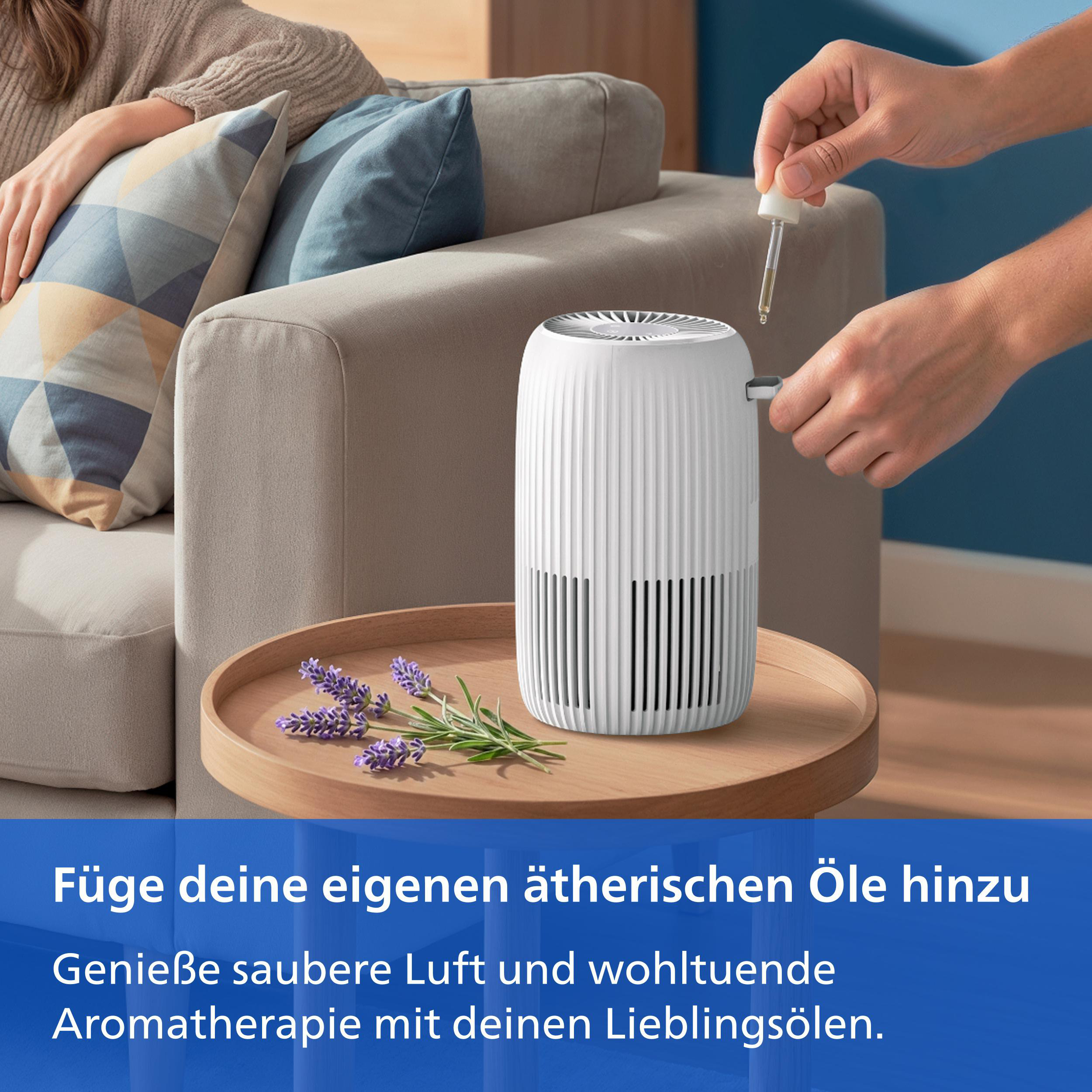 Eine Person gibt ätherisches Öl in einen weißen Luftreiniger auf einem Holztisch mit Lavendel.