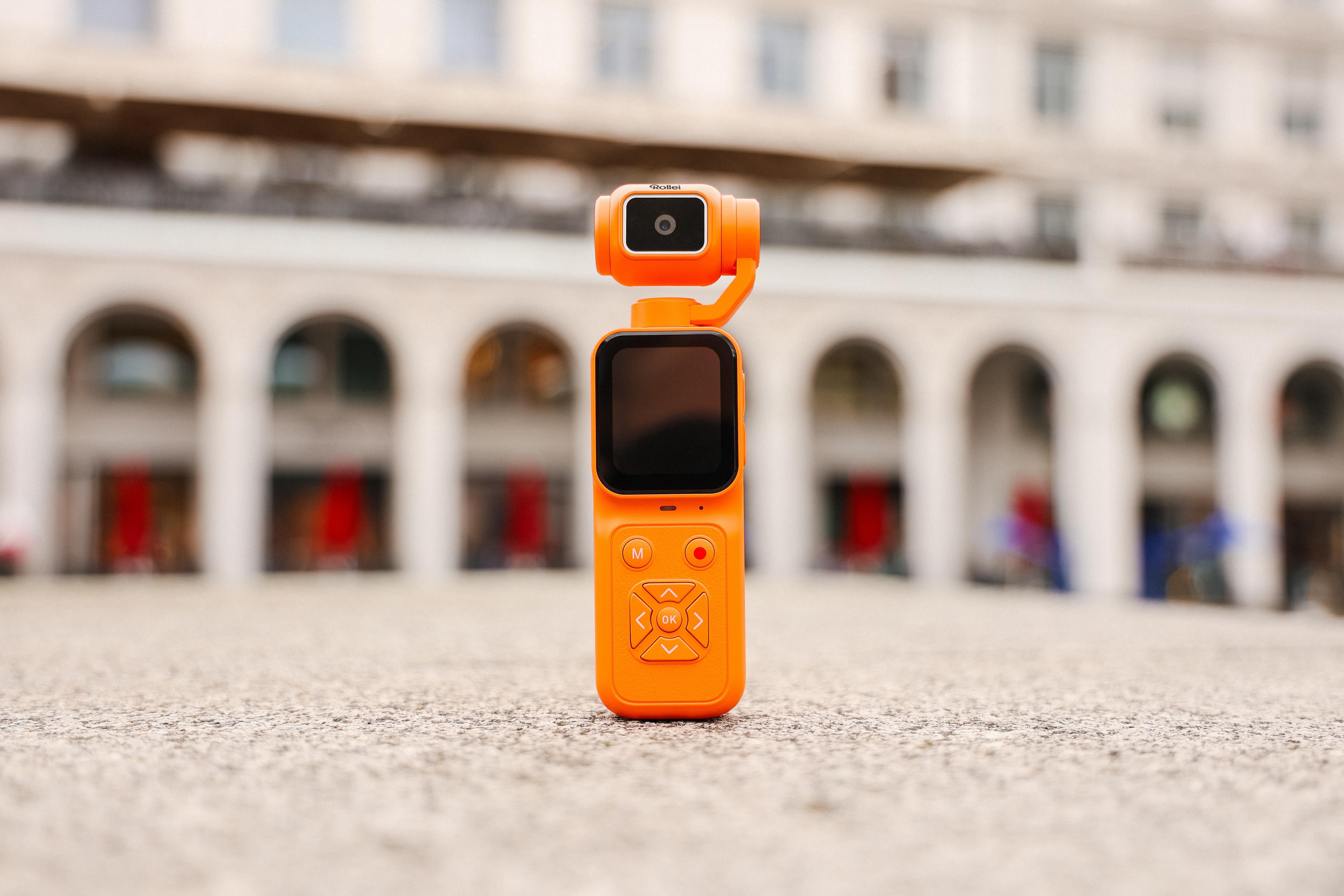 Eine orangefarbene Gimbal-Kamera steht im Fokus vor einer unscharfen historischen Arkadenfassade.
