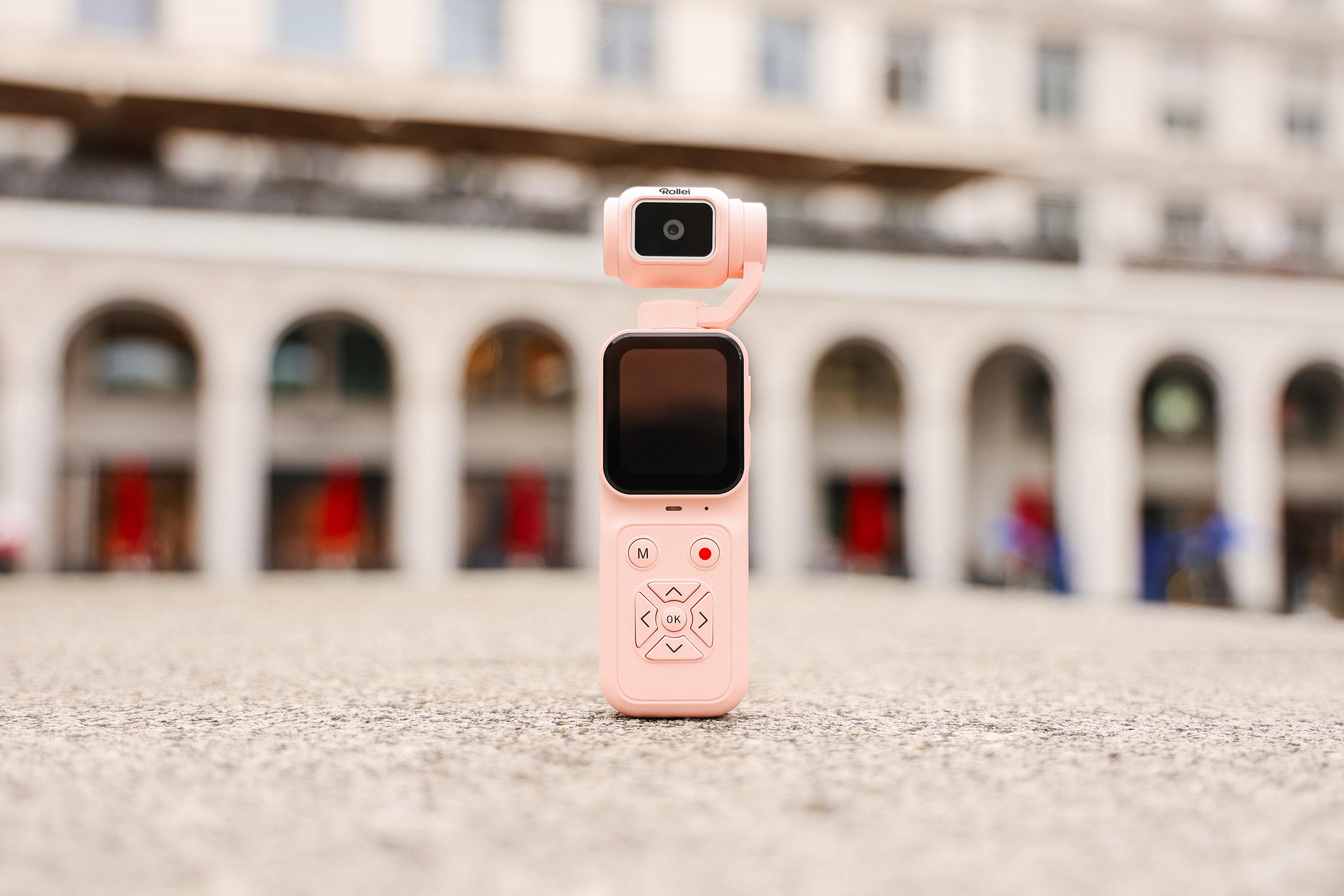 Eine rosa Gimbal-Kamera steht auf Steinboden vor einem Gebäude mit Säulen.