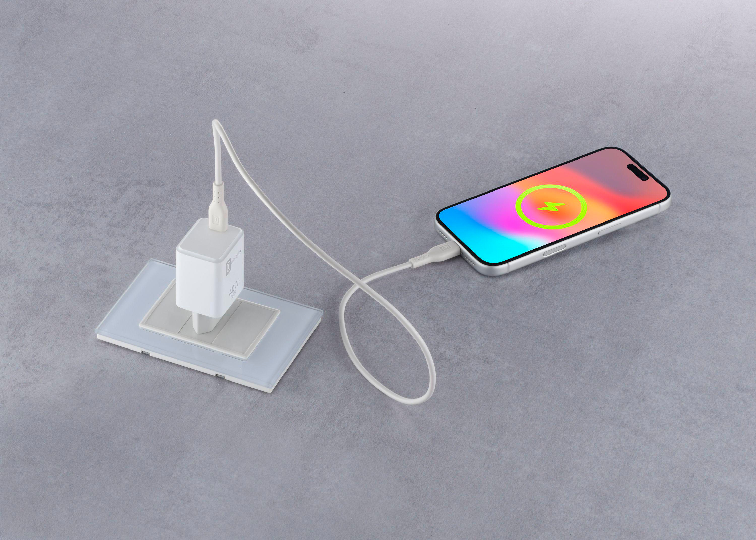 Ein Smartphone lädt auf einer grauen Oberfläche über ein weißes Kabel an einem Wandladegerät.