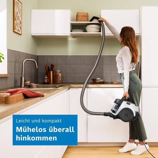 Eine Frau nutzt einen kompakten Staubsauger, um ein oberes Küchenregal zu reinigen.