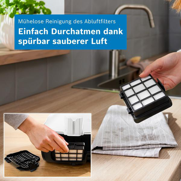 Eine Person hält einen schwarzen Staubsaugerfilter über eine Küchentheke, mit Detailbild.