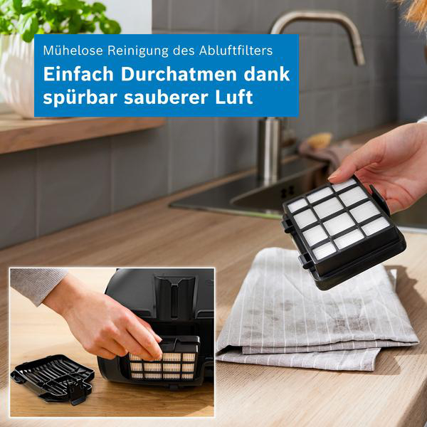 Eine Hand hält einen schwarzen Staubsaugerfilter in einer modernen Küche, daneben ein graues Tuch.