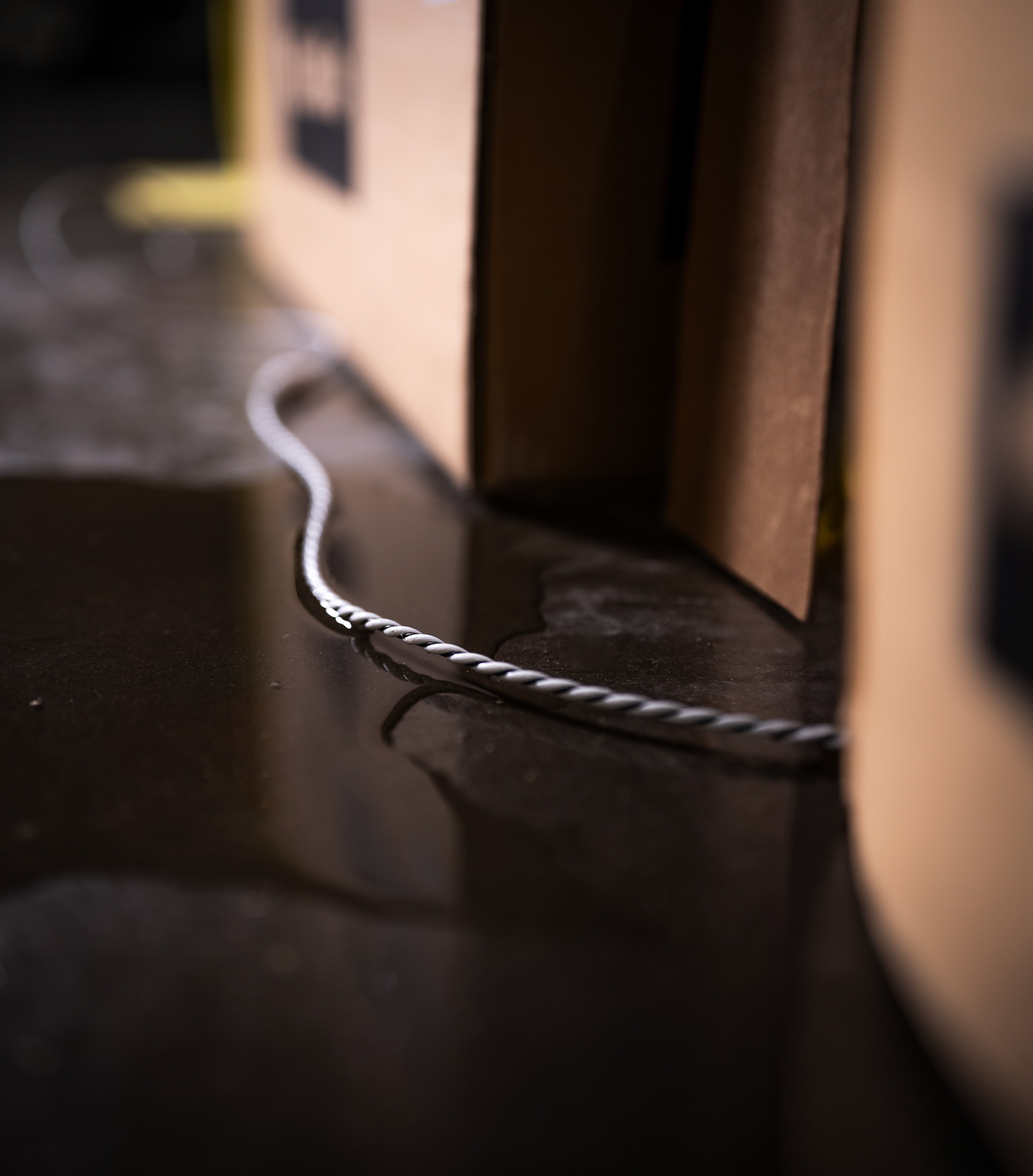 Ein weißes Kabel liegt auf dem dunklen, feuchten Boden neben braunen Kartons.