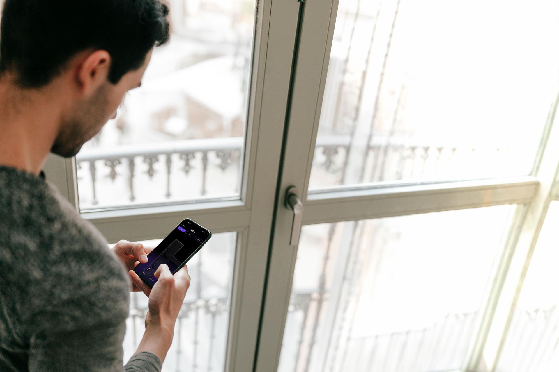 Ein Mann steht vor einem Fenster und benutzt eine App auf seinem Smartphone.