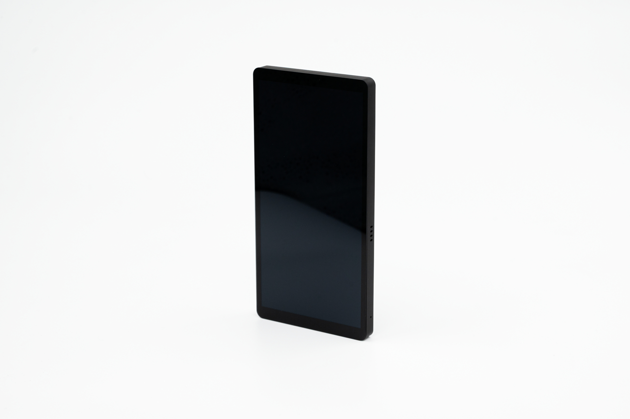 Ein schwarzes Smartphone steht aufrecht auf einer weißen Unterlage gegen einen hellen Hintergrund.