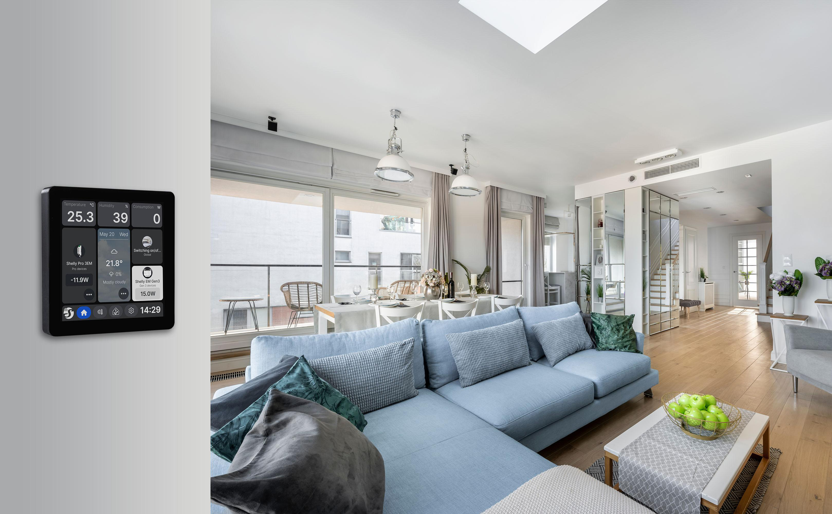 Wohnzimmer mit blauem Sofa, Kaffeetisch, grossem Fenster und digitalem Wanddisplay für Smart-Home-Steuerung.