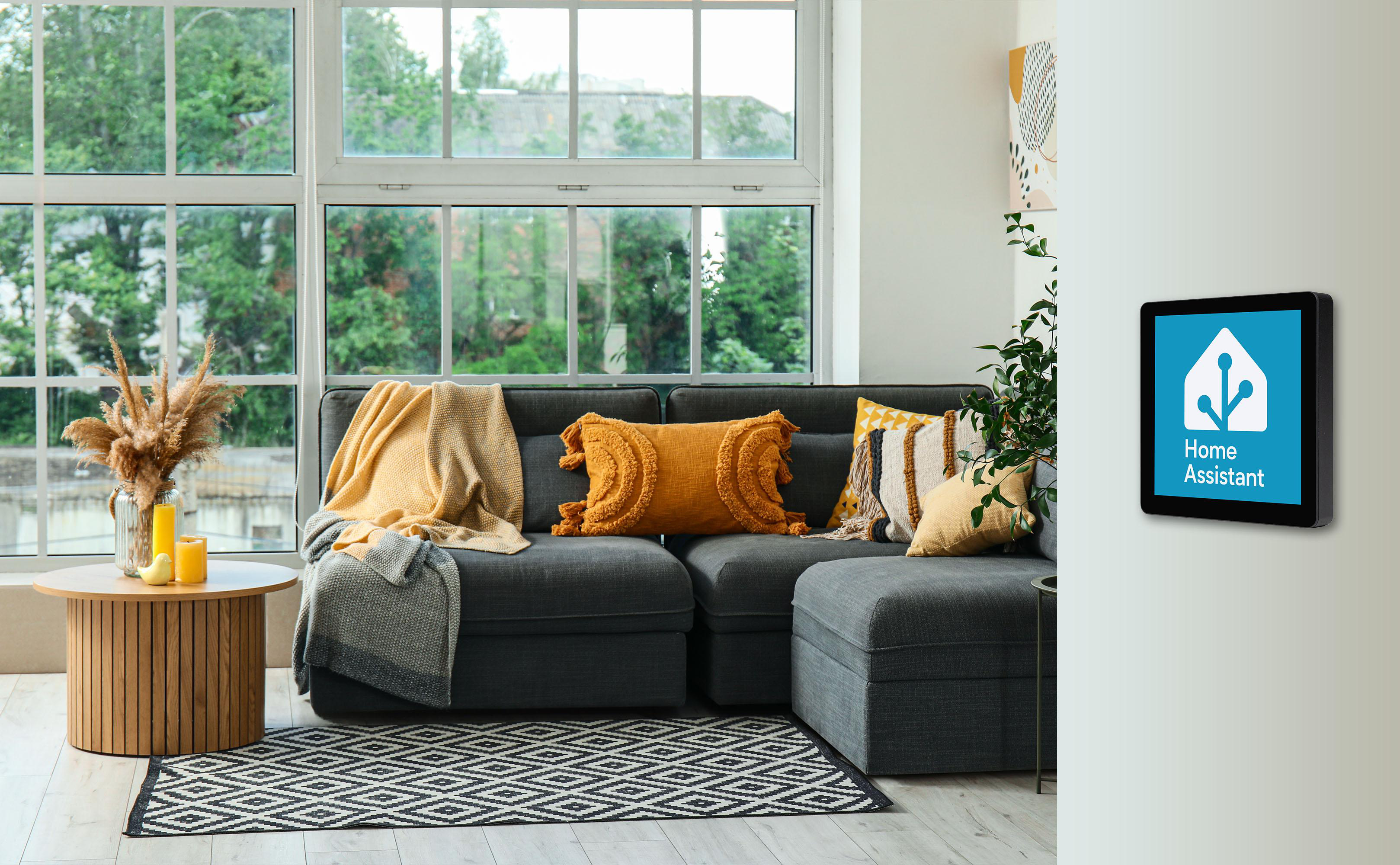 Gemütliches Wohnzimmer mit grauem Sofa, gelben Kissen und einem Home Assistant-Panel an der Wand.