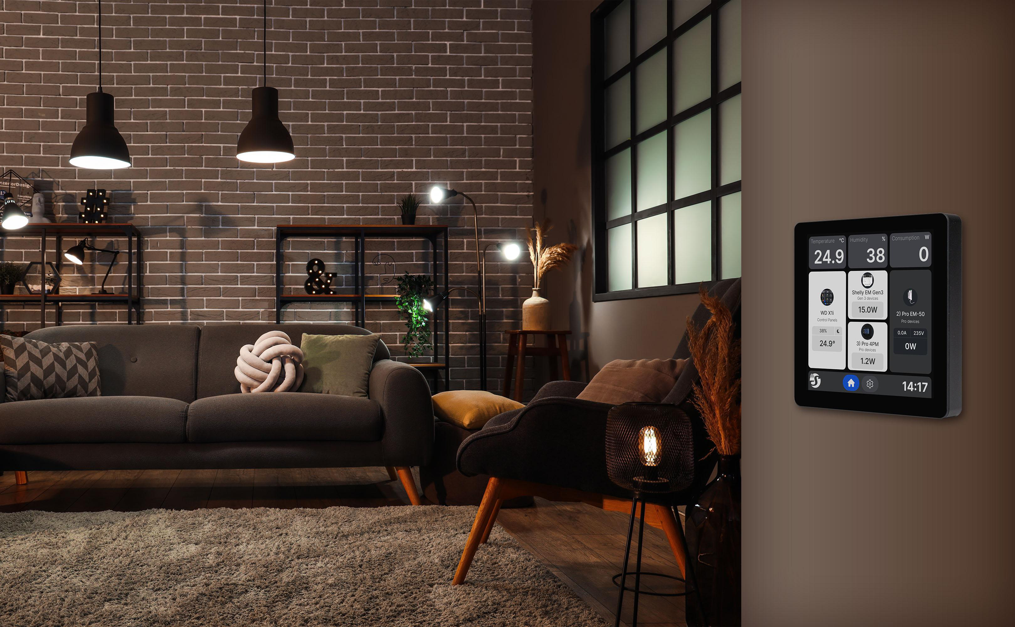 Wohnzimmer mit Ziegelwand, dunkler Couch und einem Wand-Smart-Display, das Temperatur und Verbrauch anzeigt.