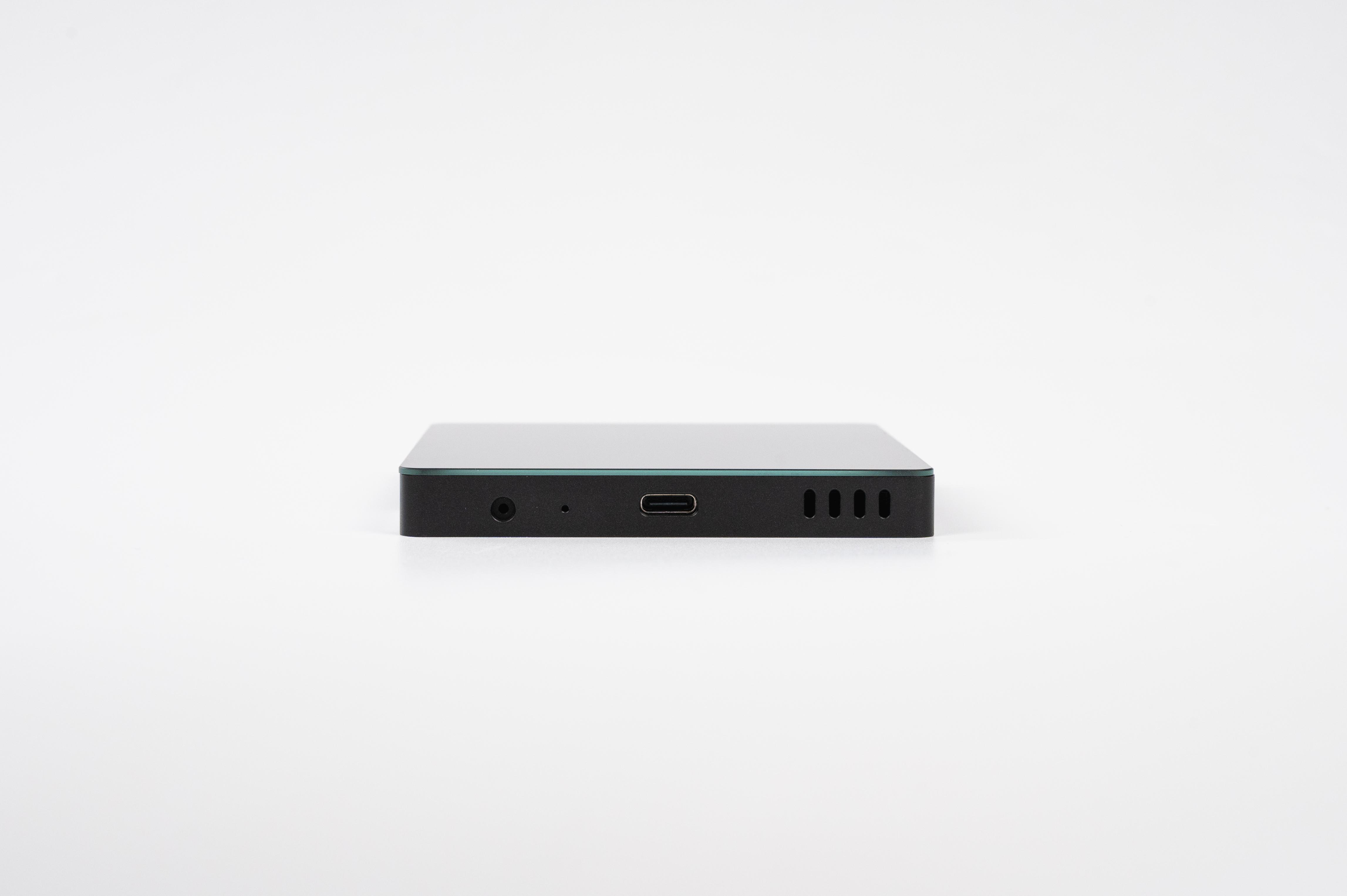Ein kleines schwarzes Gerät auf weißem Hintergrund mit einem Audioanschluss, USB-C-Anschluss und Lüftungsschlitzen.