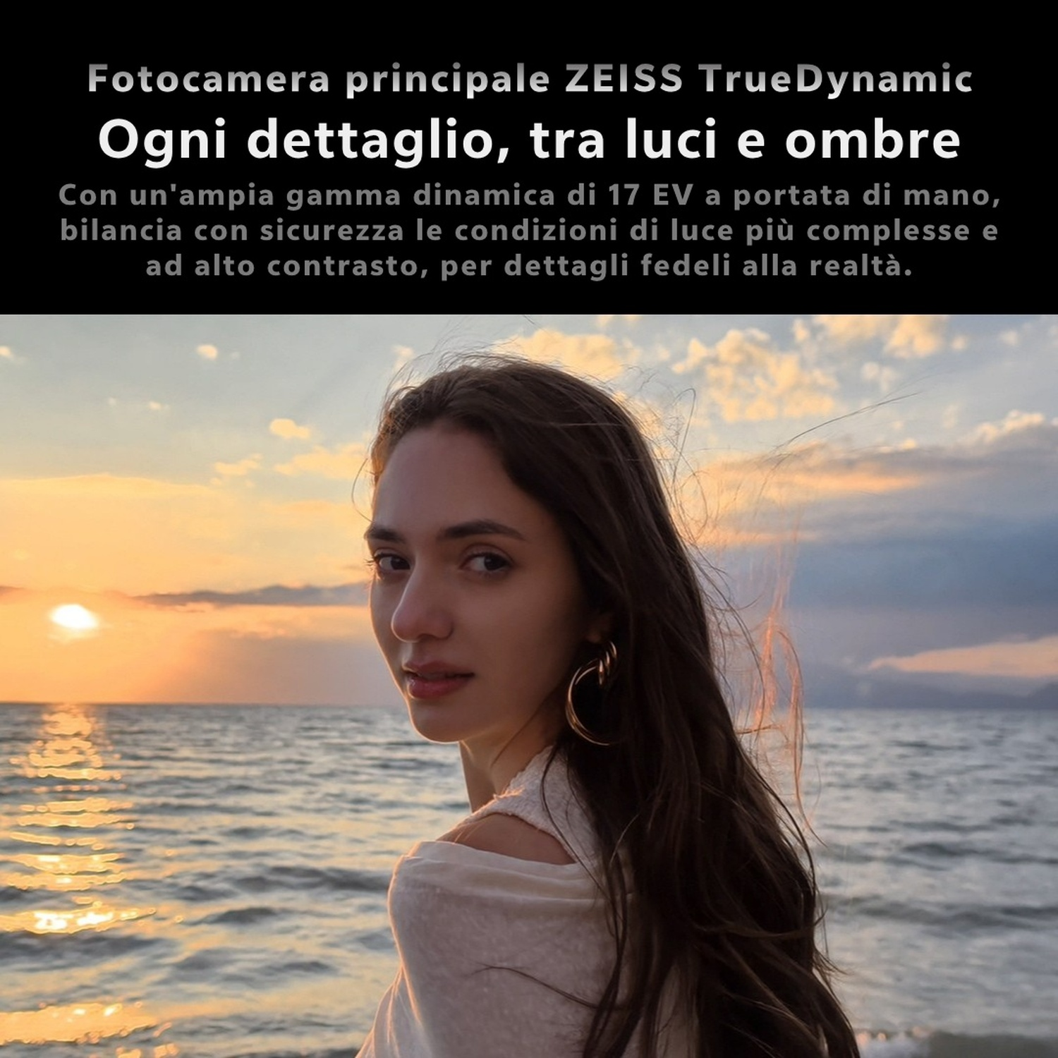 Una donna con lunghi capelli castani guarda la fotocamera davanti a un tramonto sul mare.