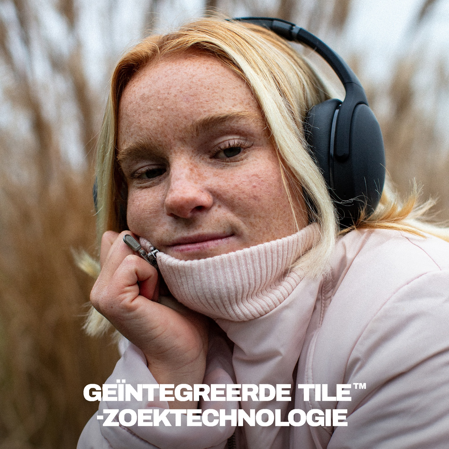 Een vrouw met sproeten, een roze coltrui en zwarte koptelefoon buiten.