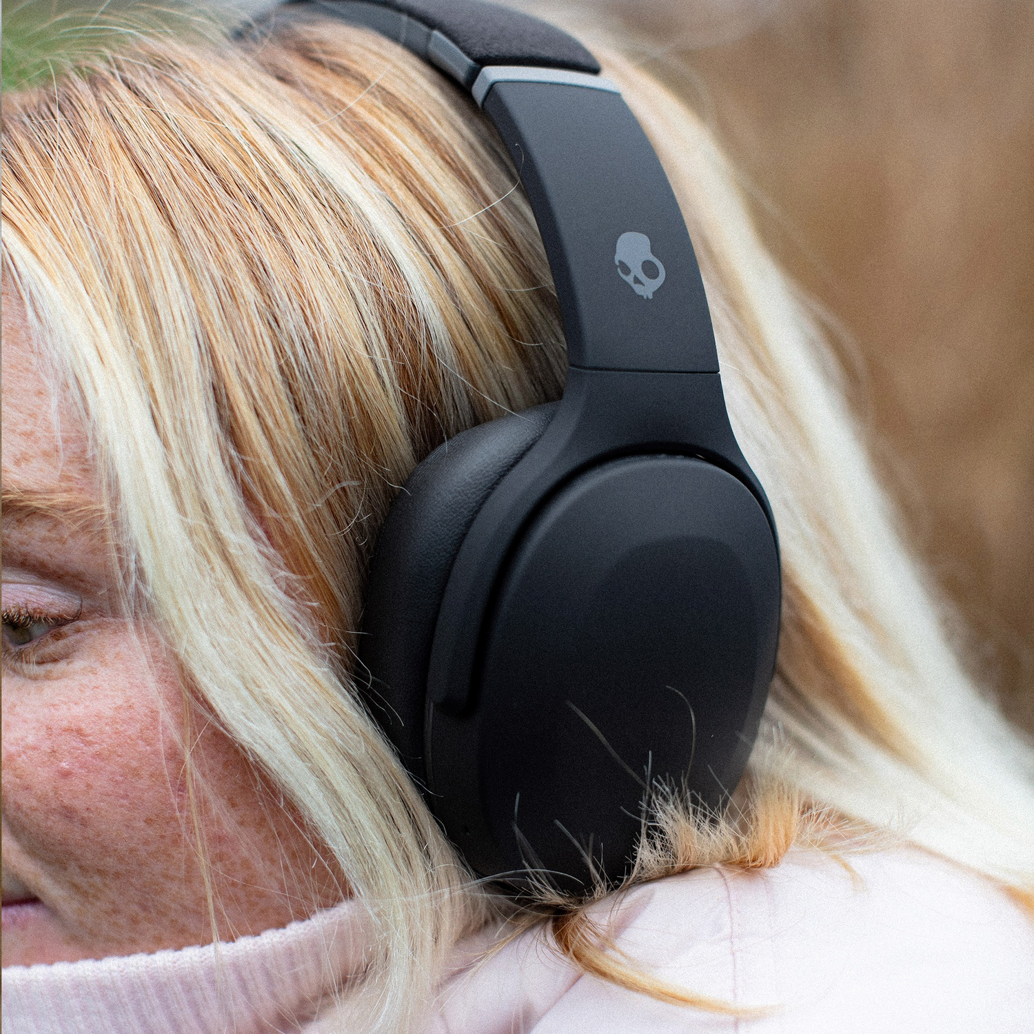 Een blonde vrouw met een grote zwarte koptelefoon met een schedellogo op de hoofdband.