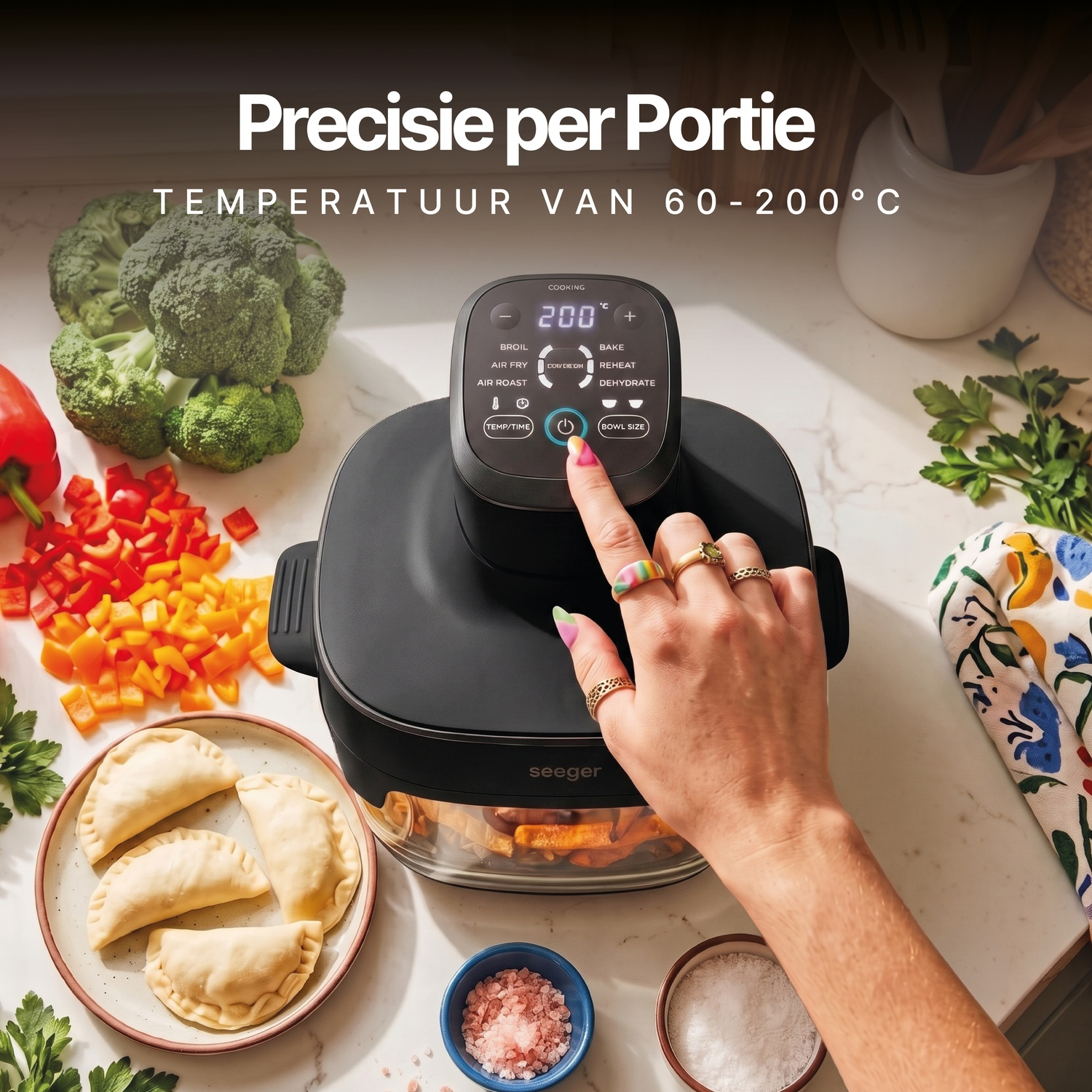 Hand drukt op de aan/uit-knop van een zwarte heteluchtfriteuse op een aanrecht met groenten en deeghapjes.