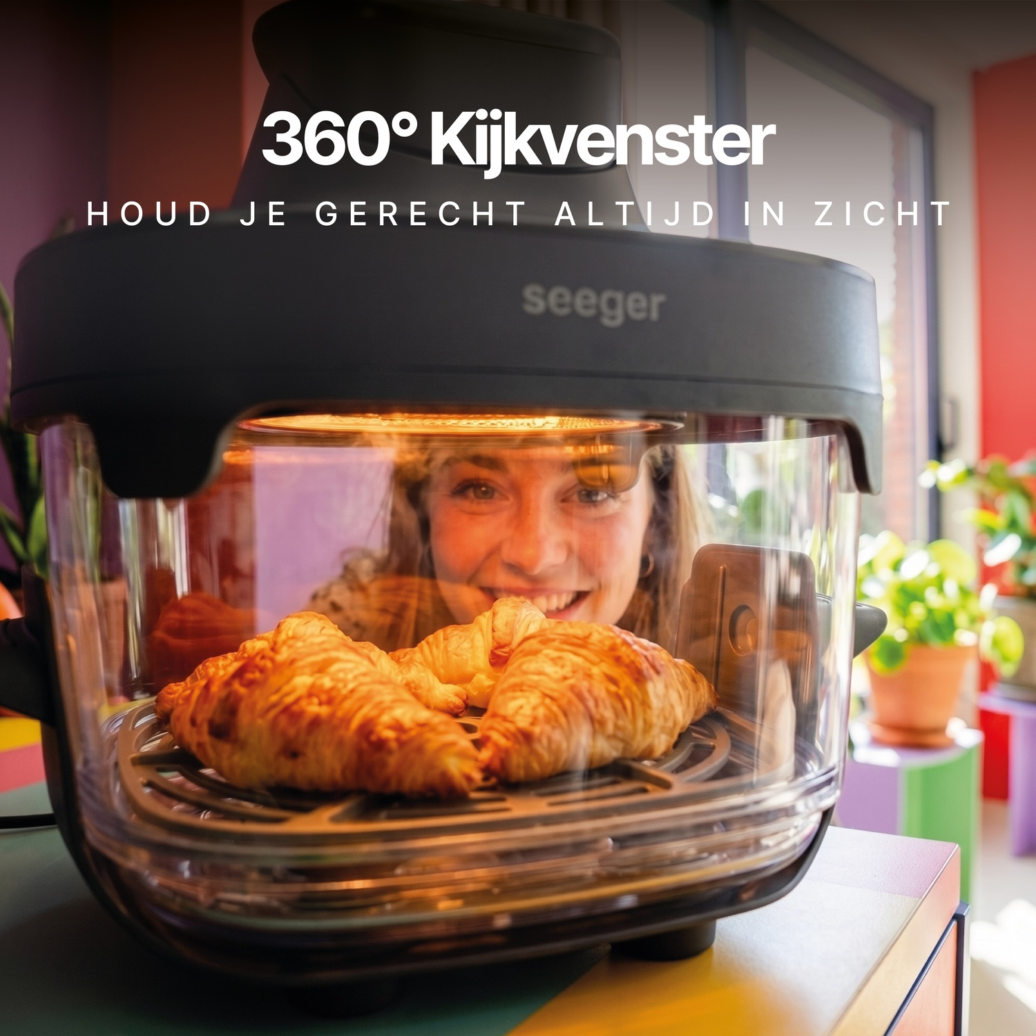 Een vrouw kijkt door het glazen venster van een zwarte heteluchtfriteuse met croissants.