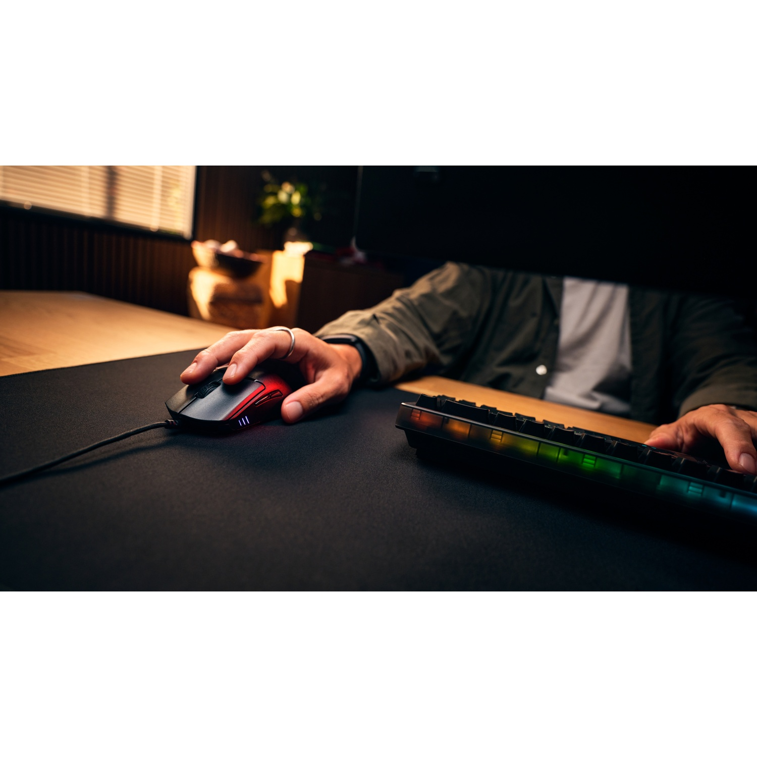 Une personne est assise à un bureau, utilisant une souris de jeu et un clavier lumineux.